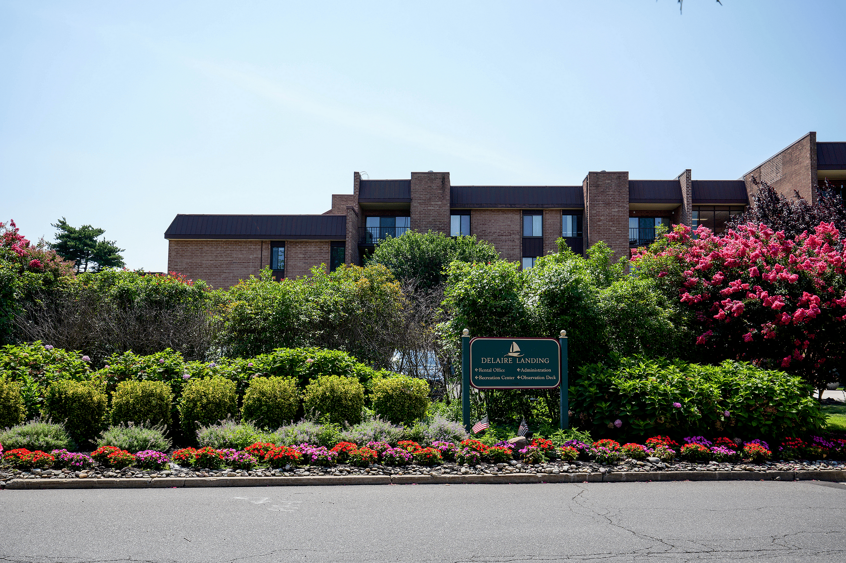 Charming apartment complex at Delaire Landing with lush greenery, vibrant flower beds, and a welcoming sign, offering a serene and inviting atmosphere.