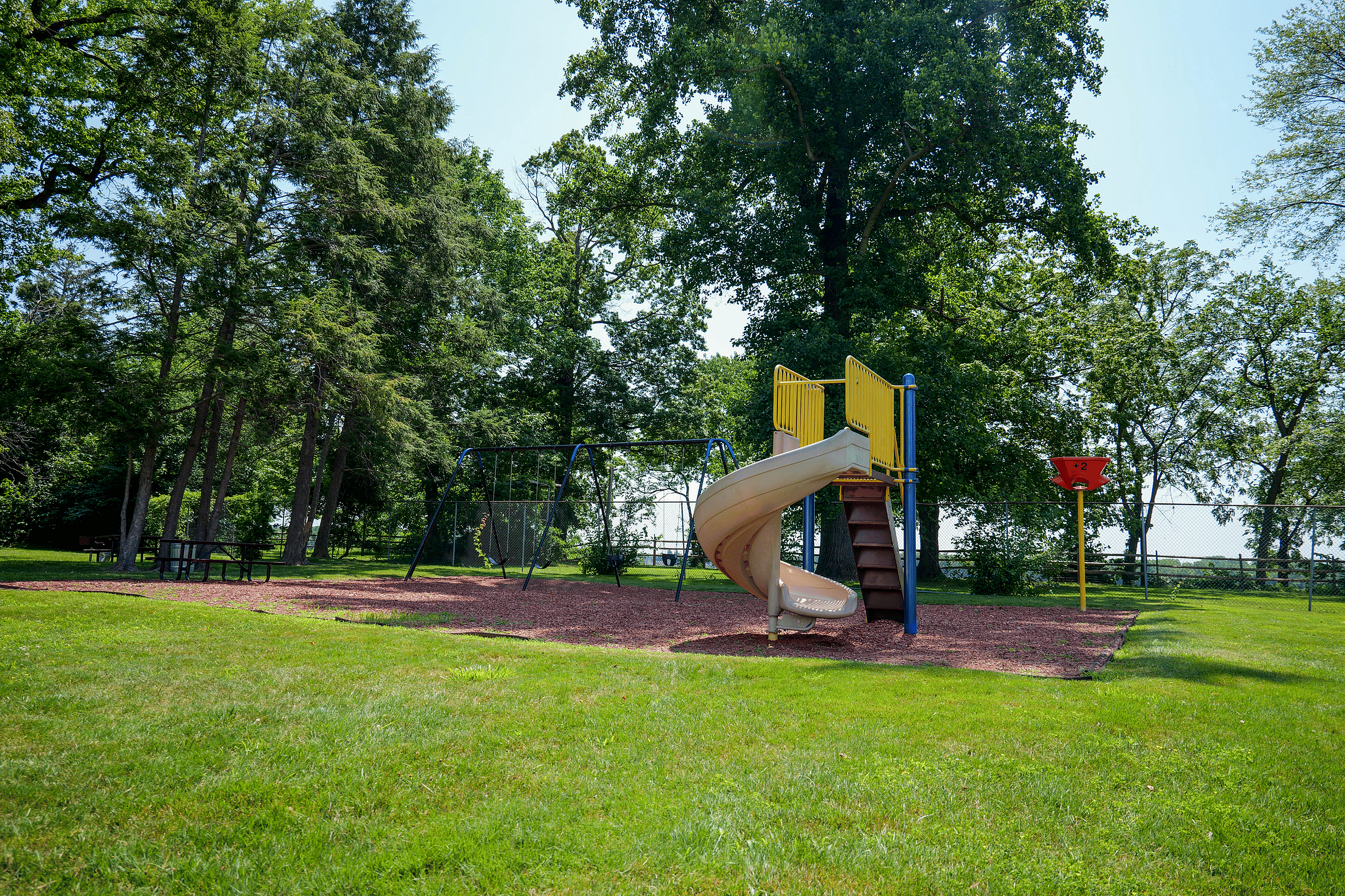 Charming playground with slide and swing set surrounded by lush greenery, perfect for family fun and outdoor activities.