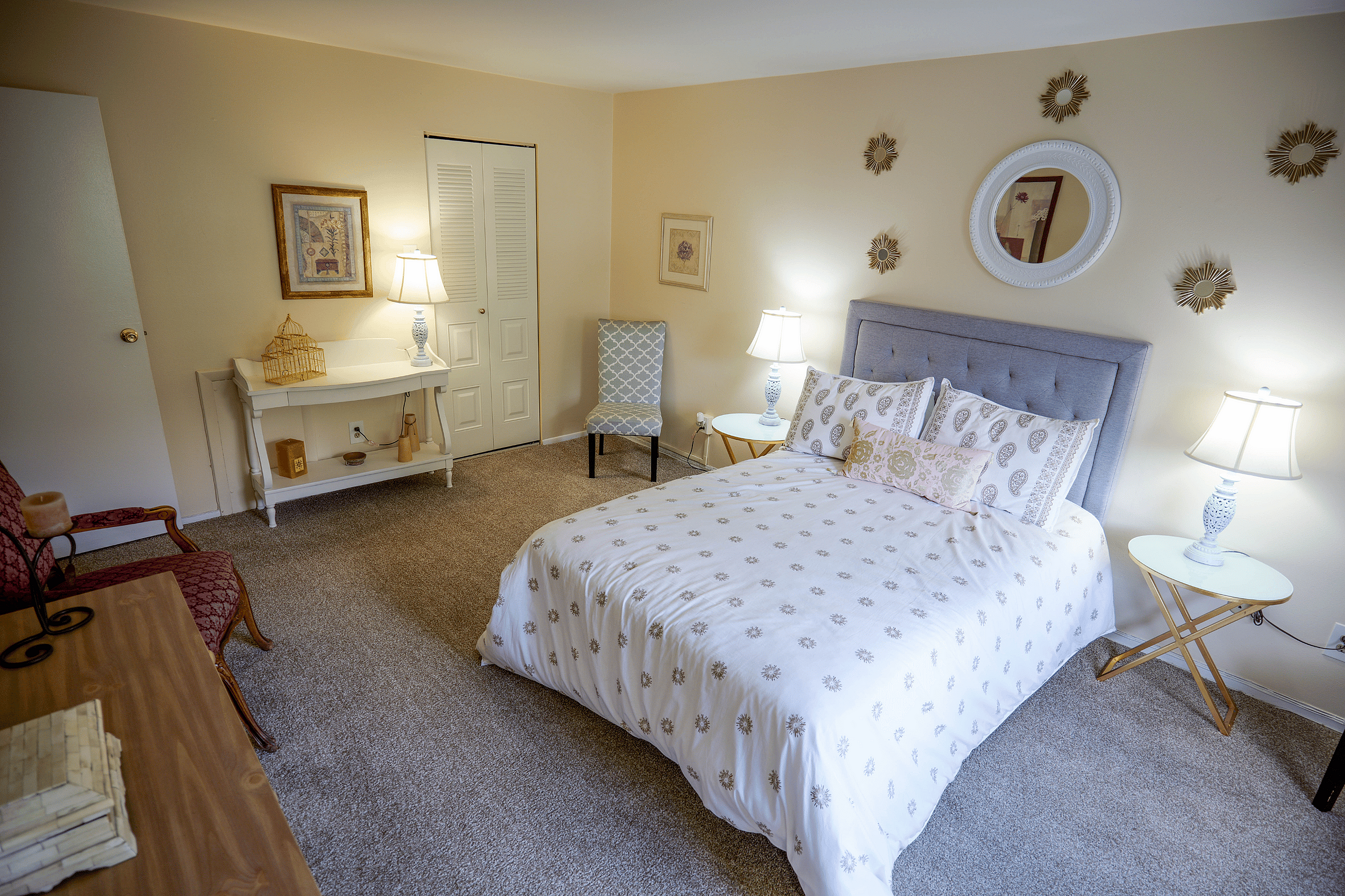 Inviting bedroom with elegant decor, featuring a plush gray headboard, patterned bedding, and warm lighting creating a cozy ambiance.