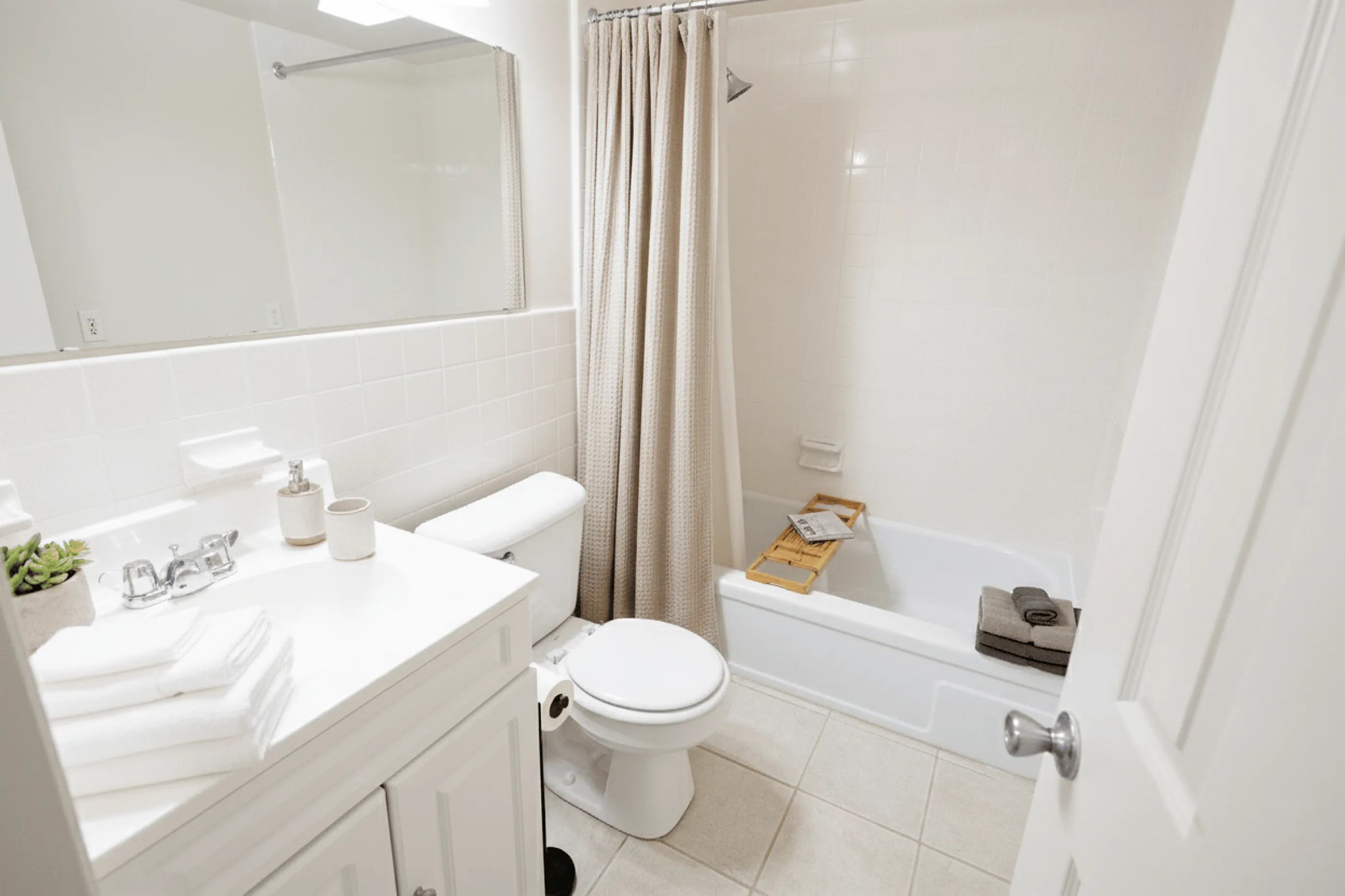 Bright, modern bathroom with elegant tile flooring, a sleek vanity, and a cozy bathtub with shower.