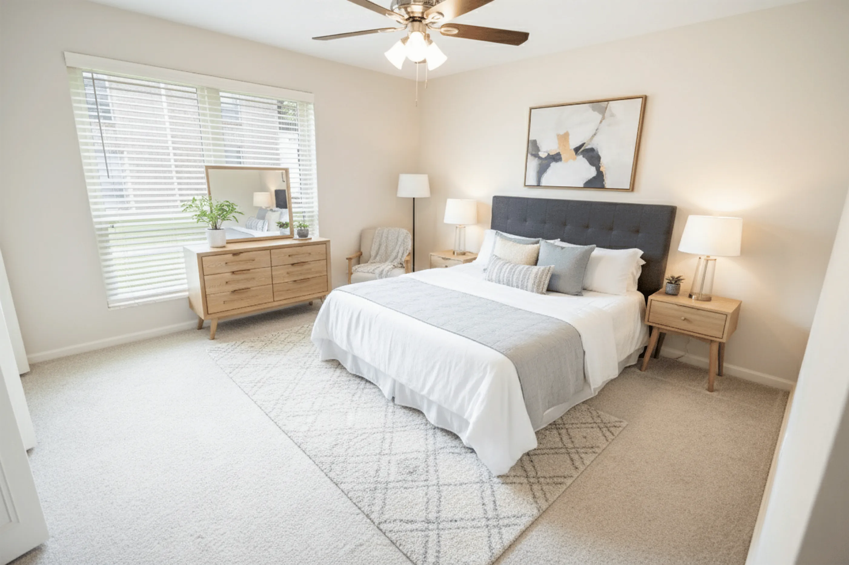 Elegant bedroom featuring a plush bed with a gray headboard, stylish wooden furniture, and abundant natural light through large windows.