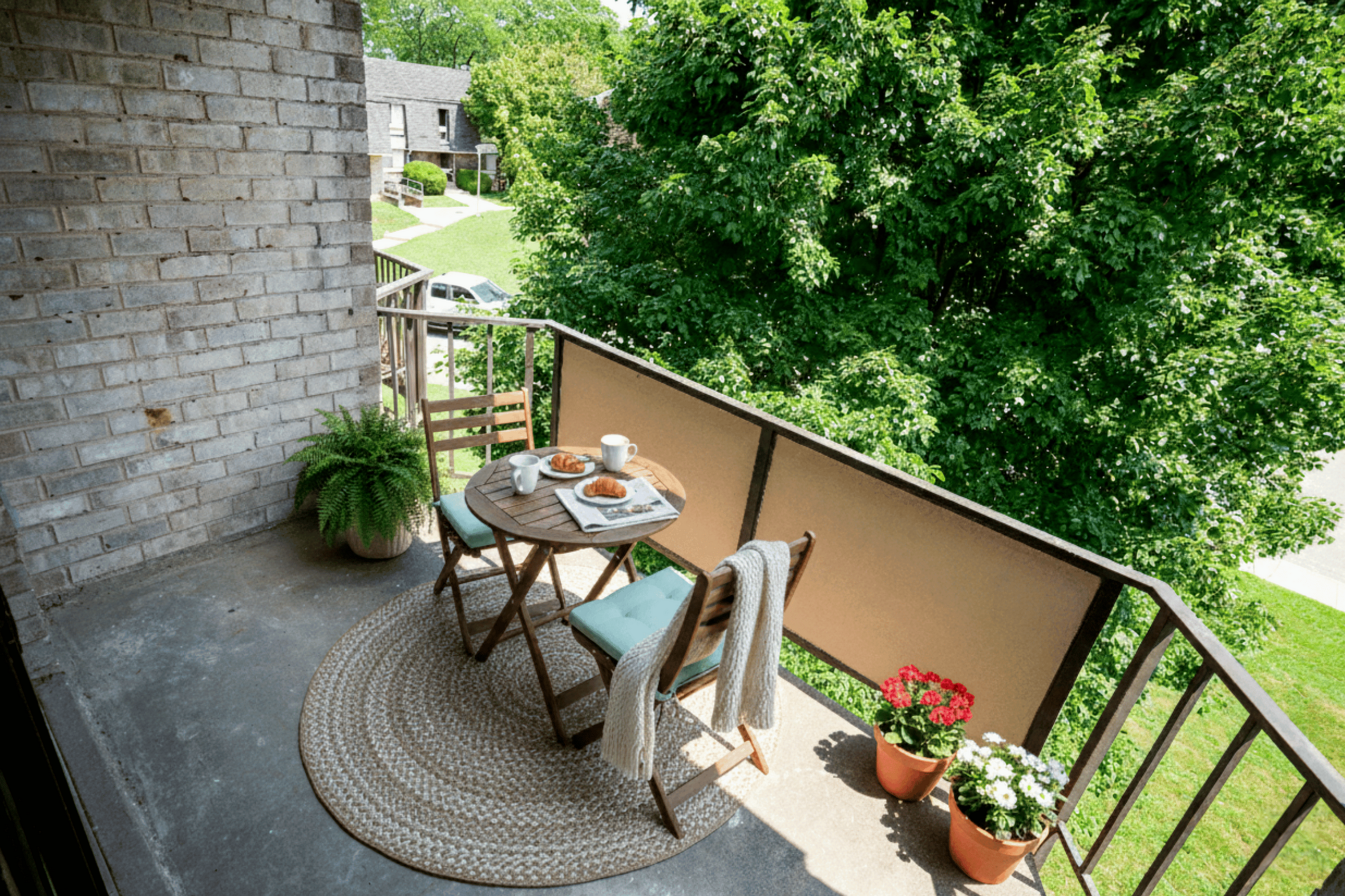 Charming balcony retreat featuring a cozy bistro set with croissants and coffee, surrounded by lush greenery and vibrant flowers.