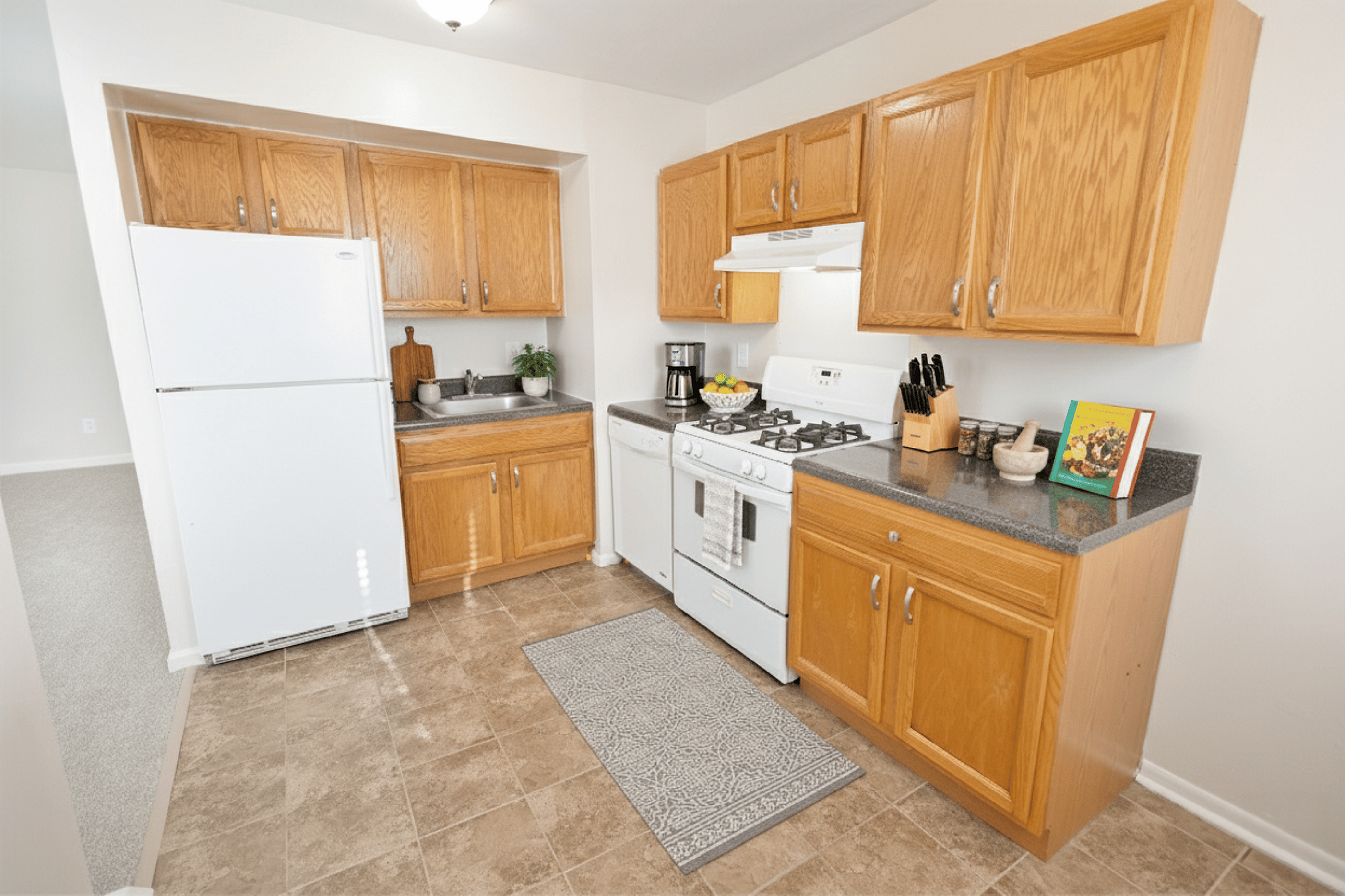 Bright and inviting kitchen with oak cabinets, modern appliances including a white fridge and gas stove, complemented by a cozy tile floor.
