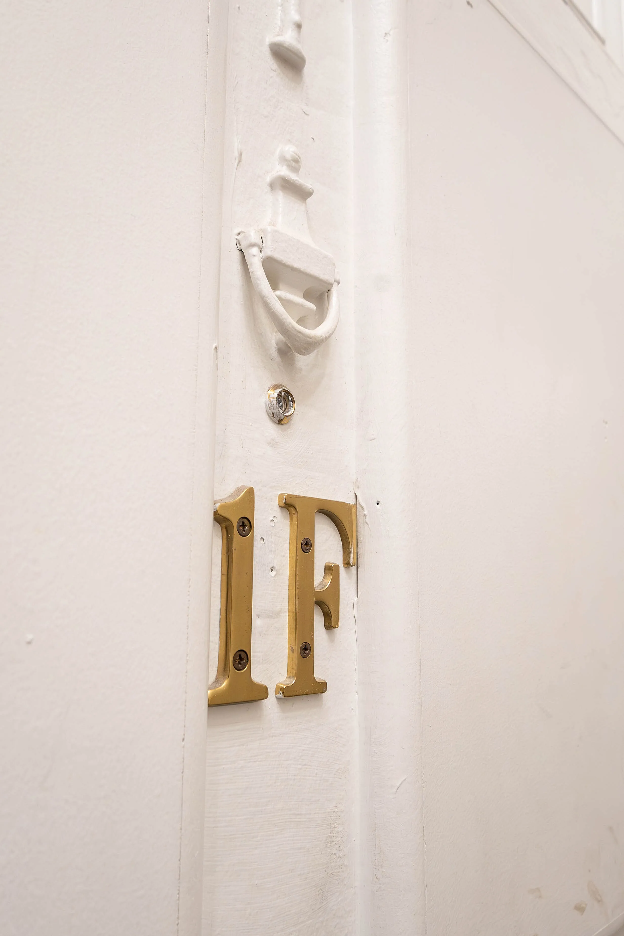 Charming white door featuring elegant gold number '1F', complemented by classic hardware, exudes a welcoming ambiance.