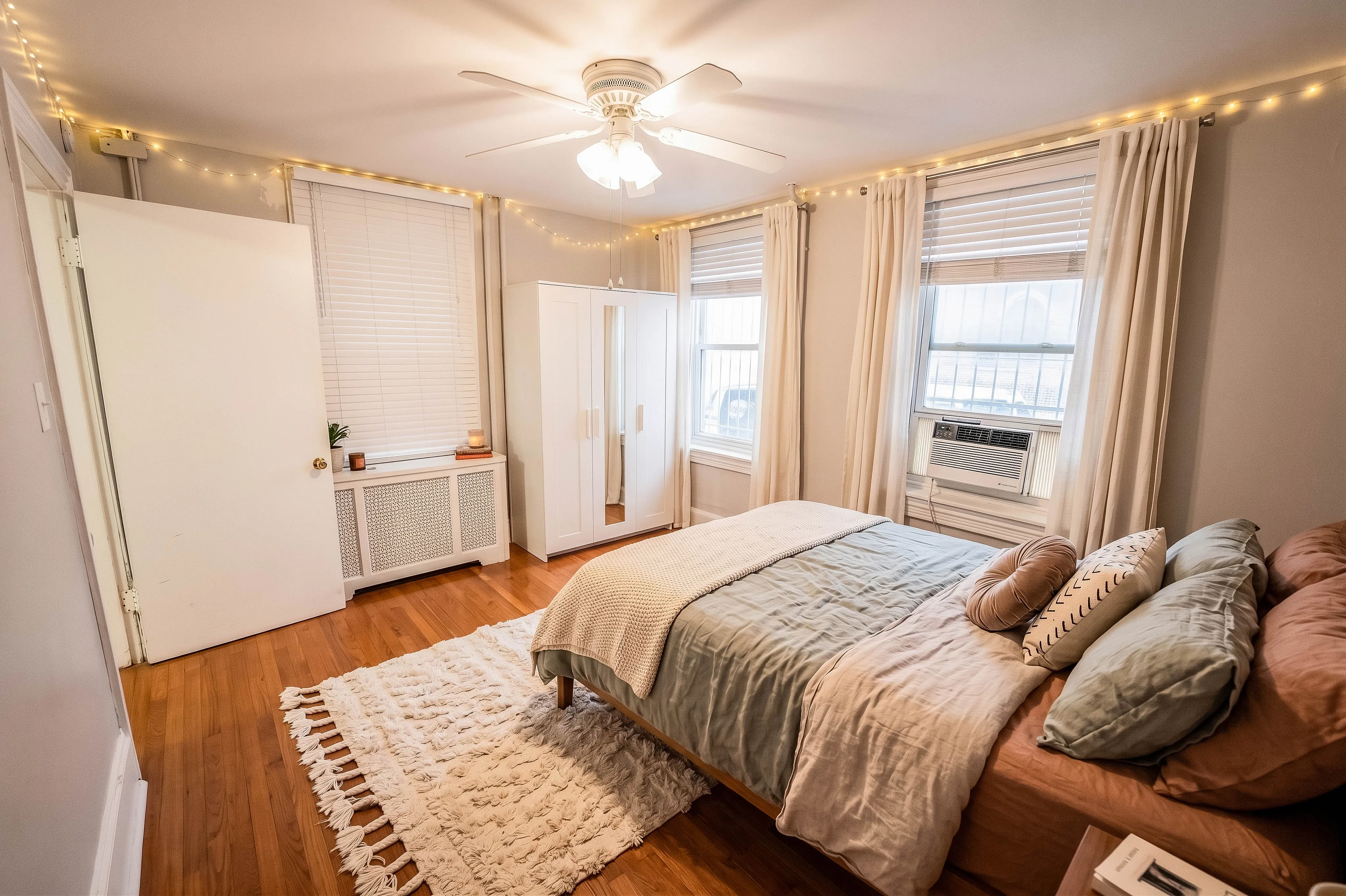 Bright and inviting bedroom with hardwood floors, cozy bedding, and natural light from multiple windows.