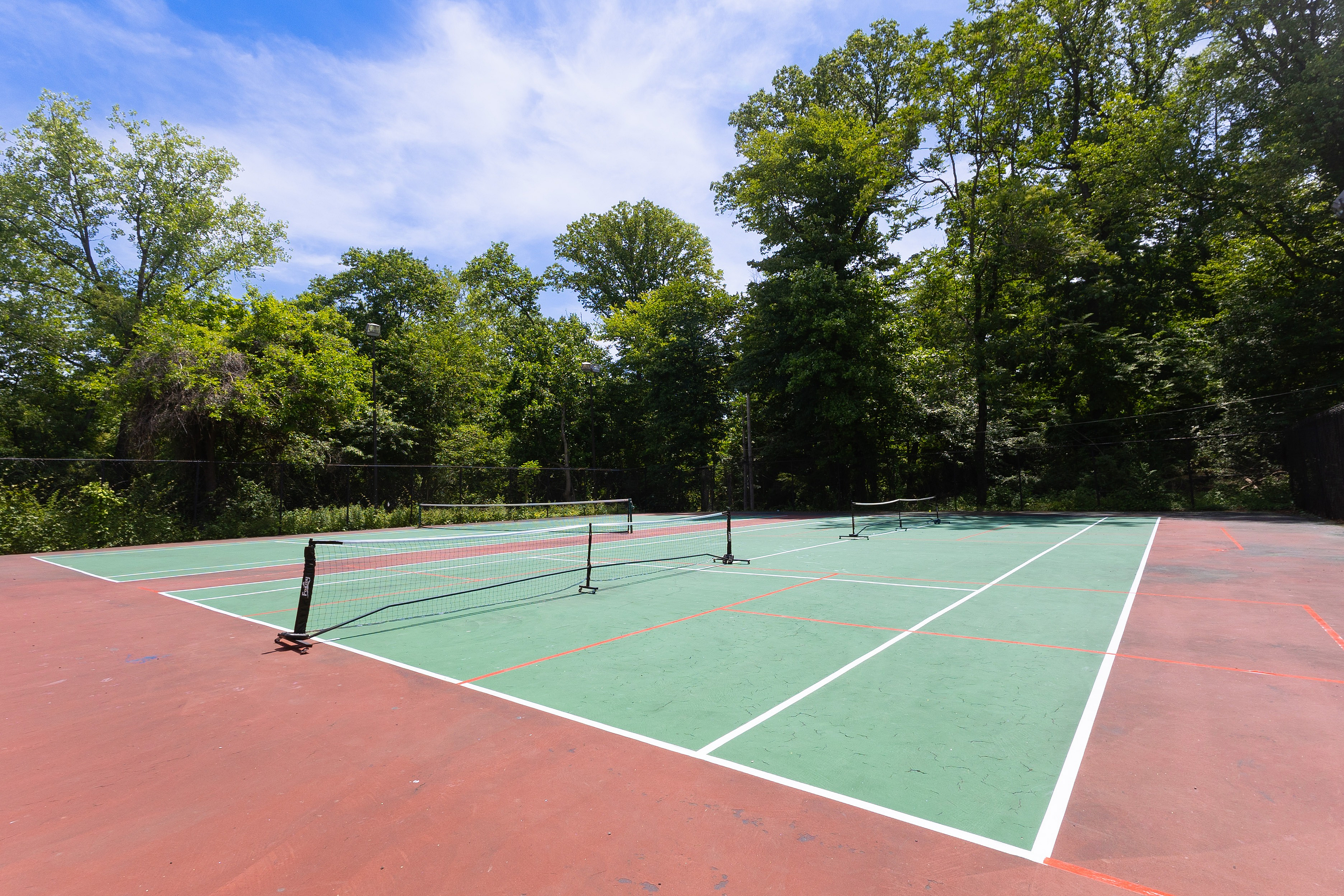 Vibrant outdoor tennis court surrounded by lush greenery and sunny blue skies, offering a perfect recreational escape.