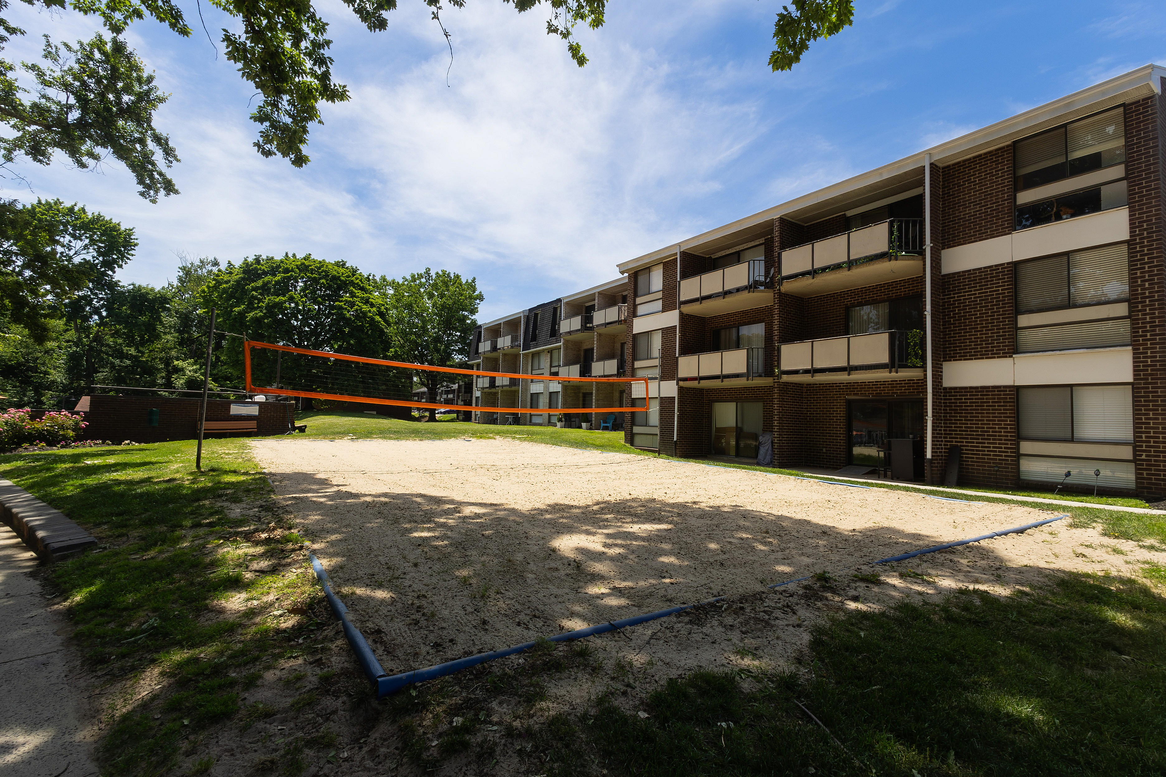 Charming apartment complex with a sand volleyball court, surrounded by lush greenery and modern balconies.