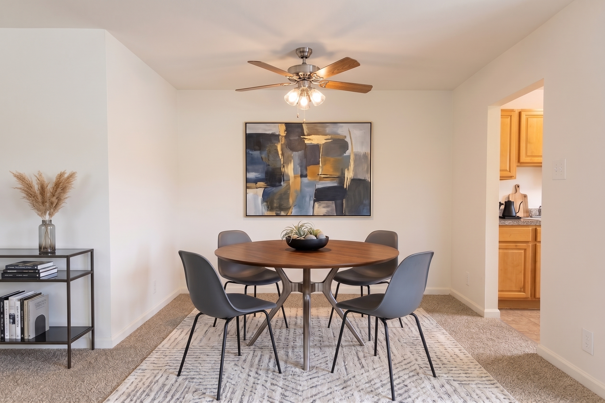 Elegant dining area with a round wooden table, modern gray chairs, and stylish abstract artwork, adjacent to a cozy kitchen.