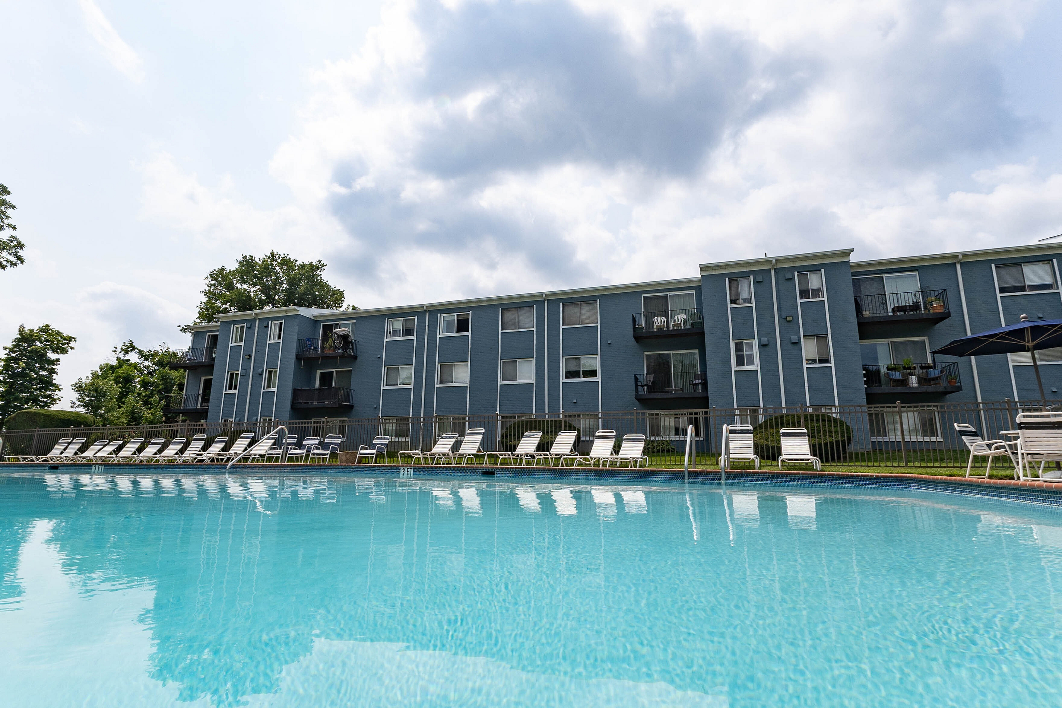 Inviting apartment complex with a sparkling blue pool, surrounded by modern buildings and lush greenery, perfect for relaxation and leisure.