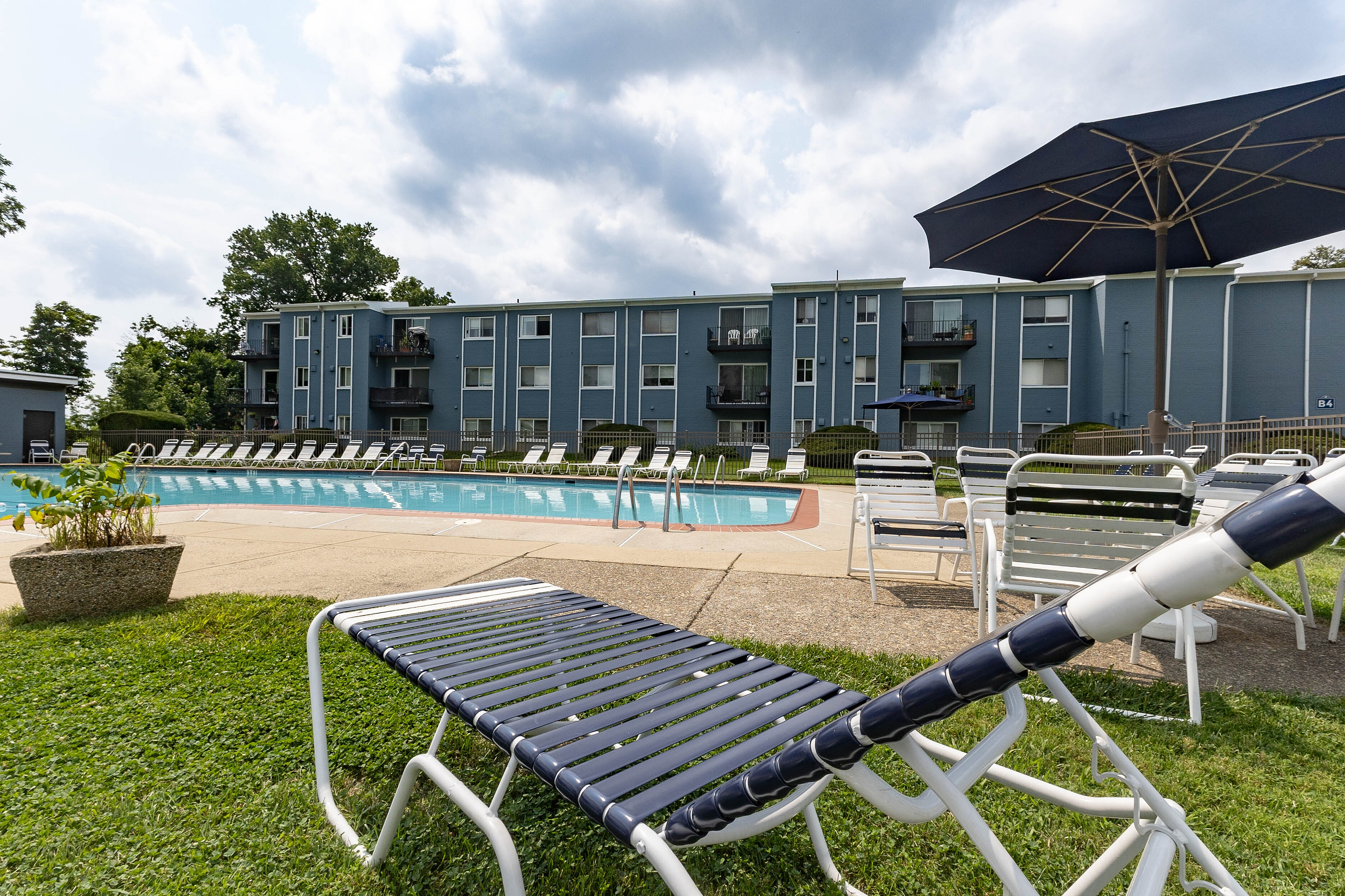 Chic apartment complex featuring a sparkling pool with relaxing loungers and modern blue façade, perfect for outdoor leisure.