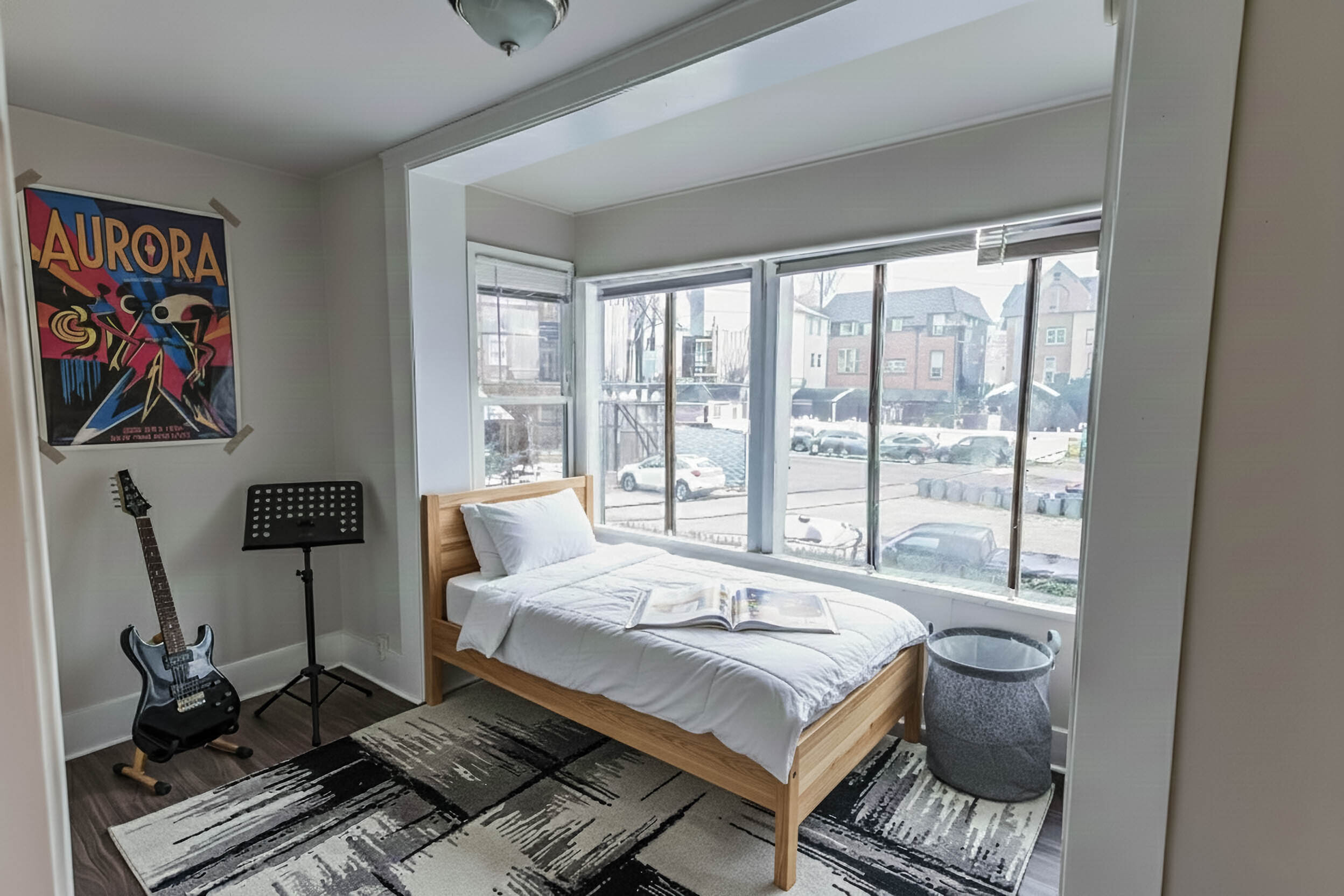 Bright bedroom showcasing a cozy single bed with modern decor, large windows offering ample sunlight, and a stylish music corner with a guitar and poster.
