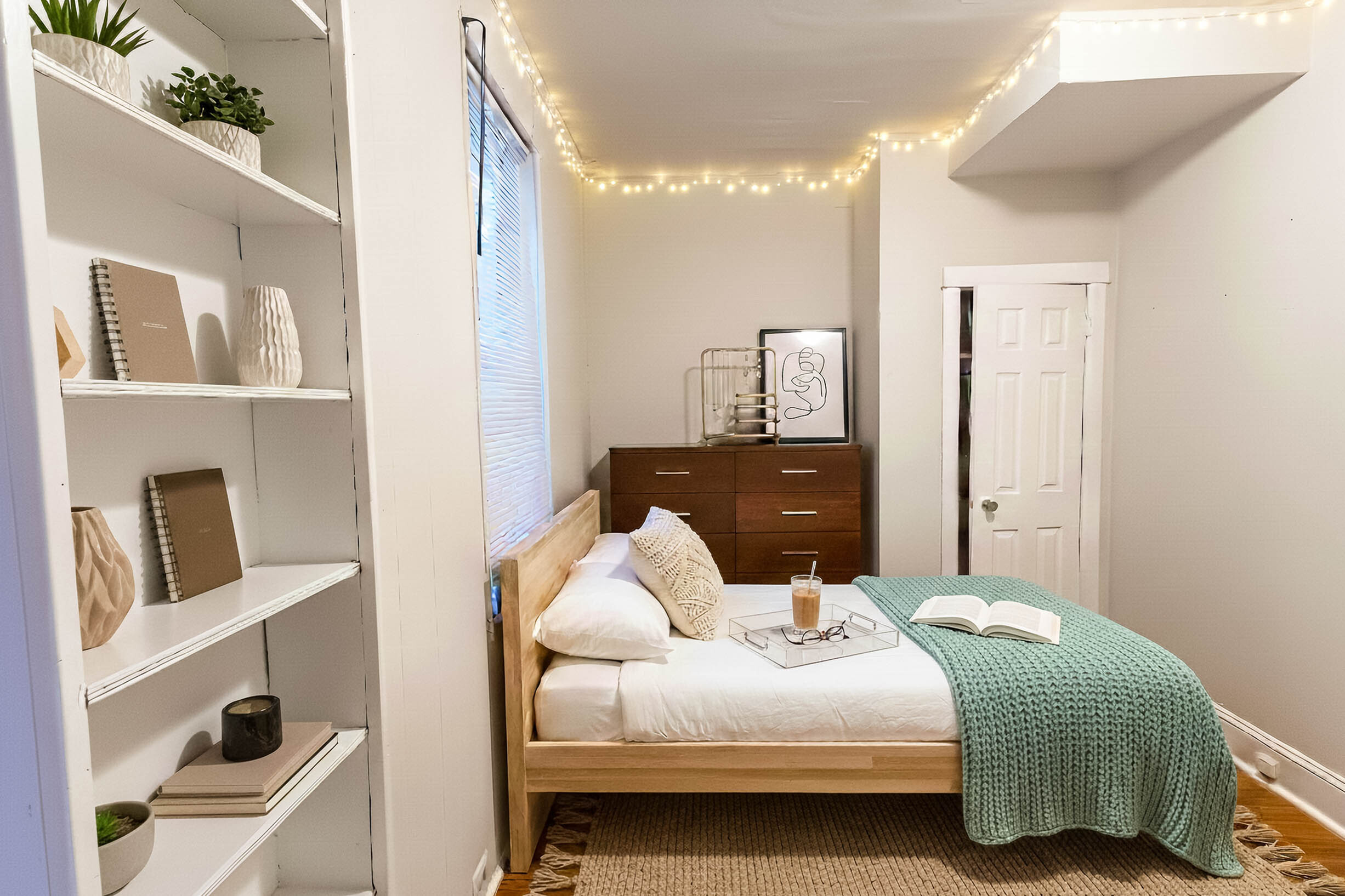 Cozy bedroom with soft string lights, elegant wood furniture, and stylish shelving. Inviting bed with a knitted throw and decorative elements create a warm and welcoming atmosphere.