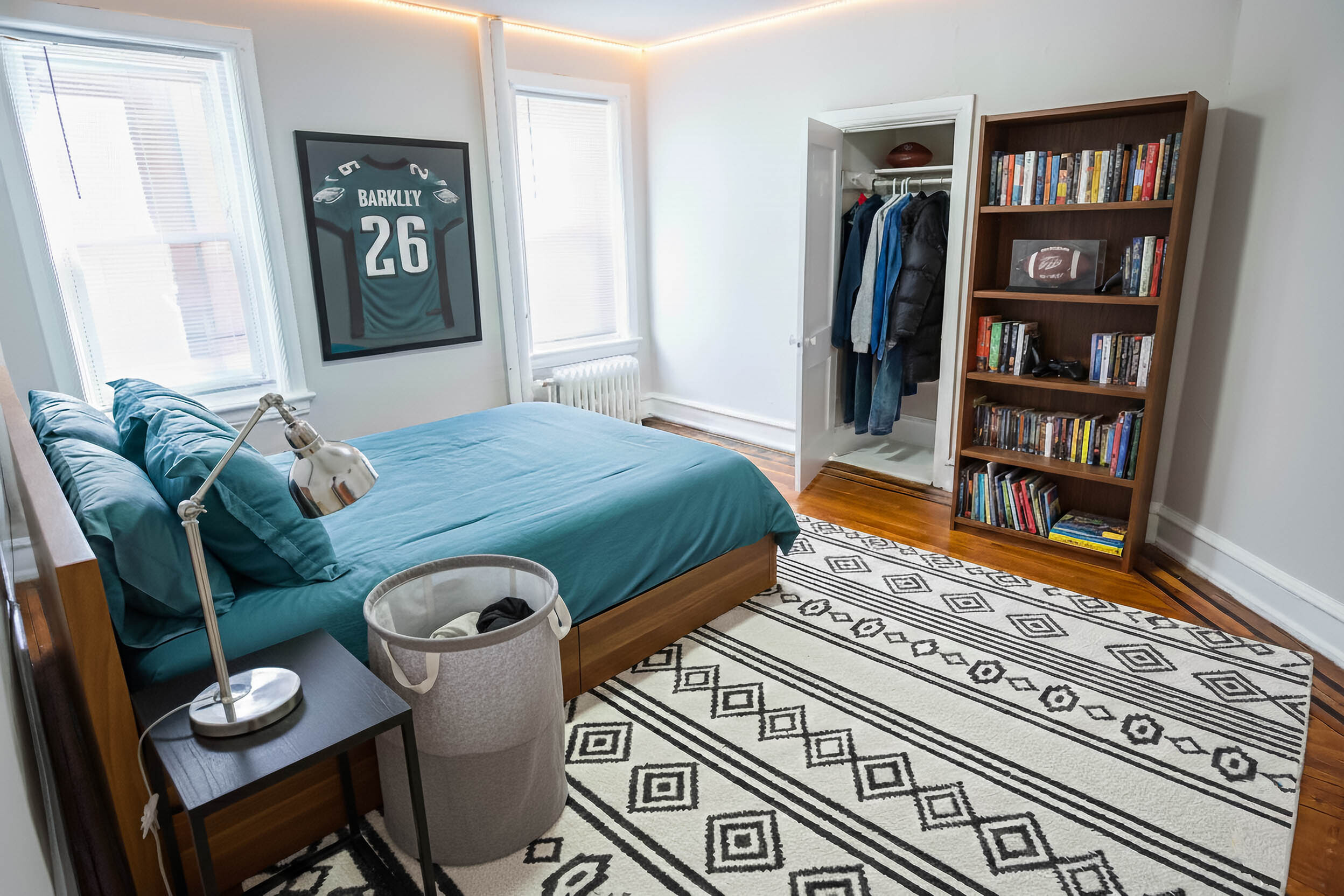 Bright and cozy bedroom featuring a blue-themed decor, sleek lighting, and a stylish wall art piece. Includes a spacious bookshelf and organized closet for optimal storage.