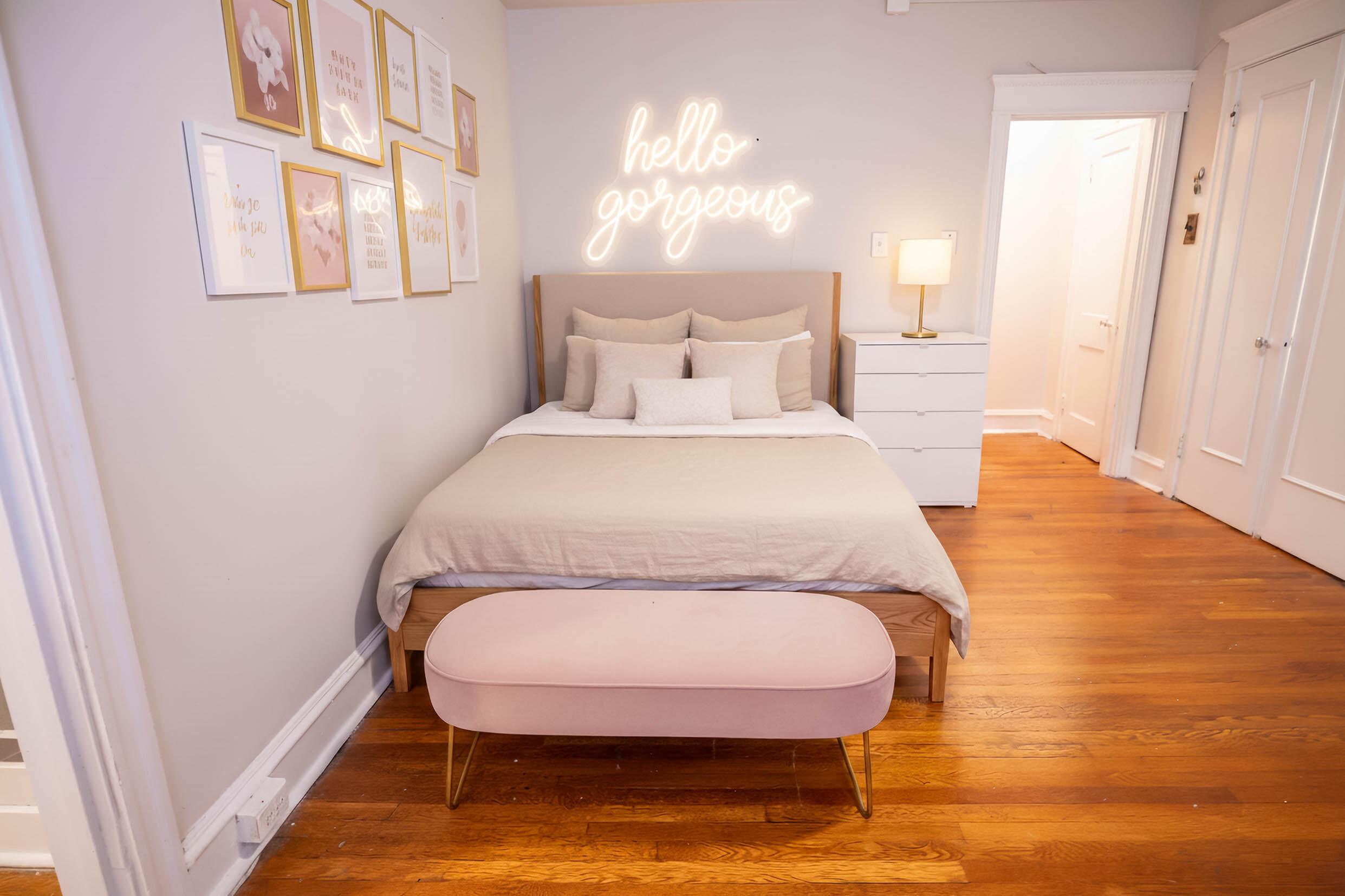Charming bedroom with cozy bed, elegant wall art, and neon \'hello gorgeous\' sign, creating a welcoming and stylish ambiance.