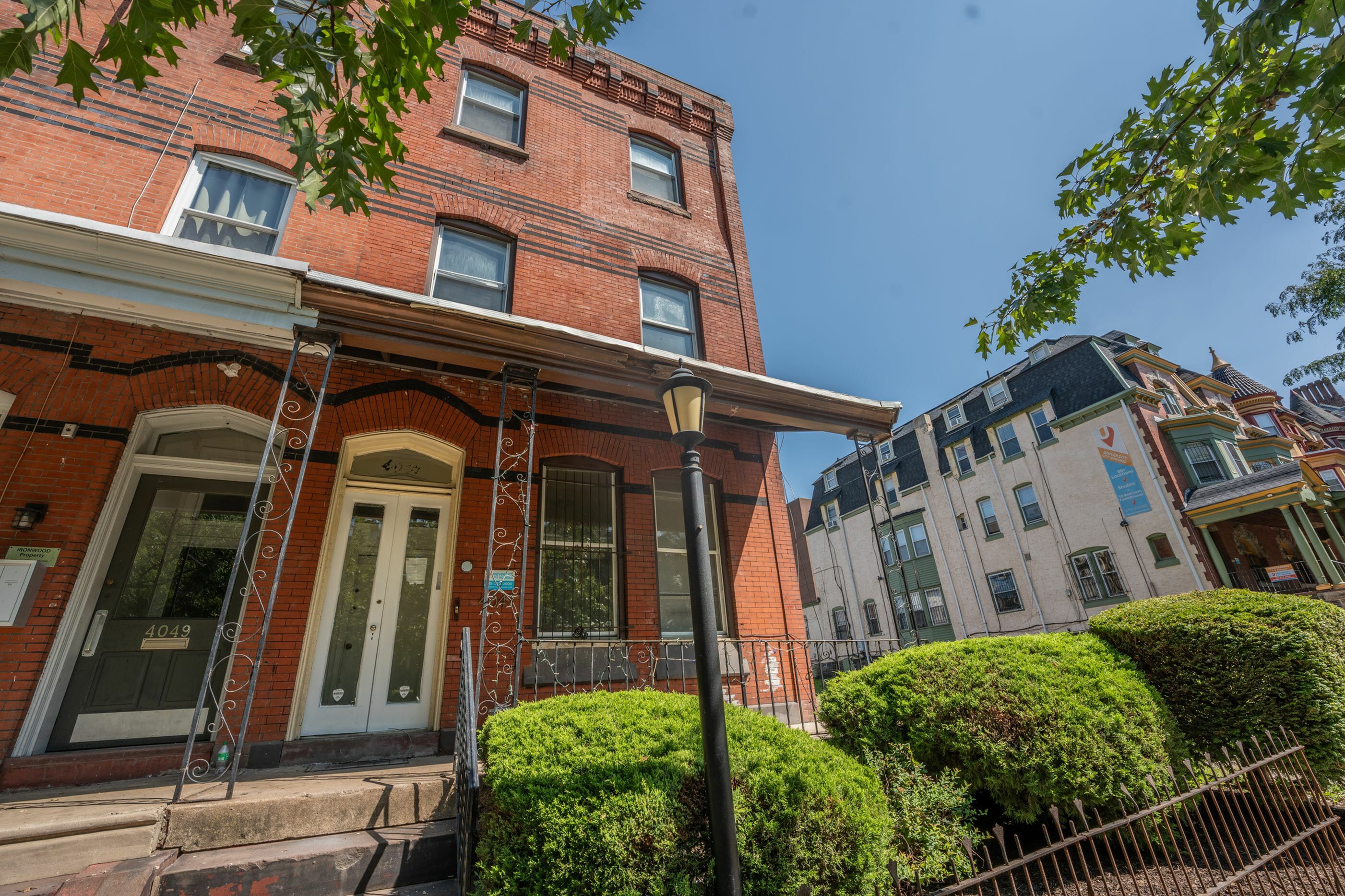 Charming red brick apartment building with a welcoming porch, complemented by neatly trimmed shrubs in a vibrant urban neighborhood.
