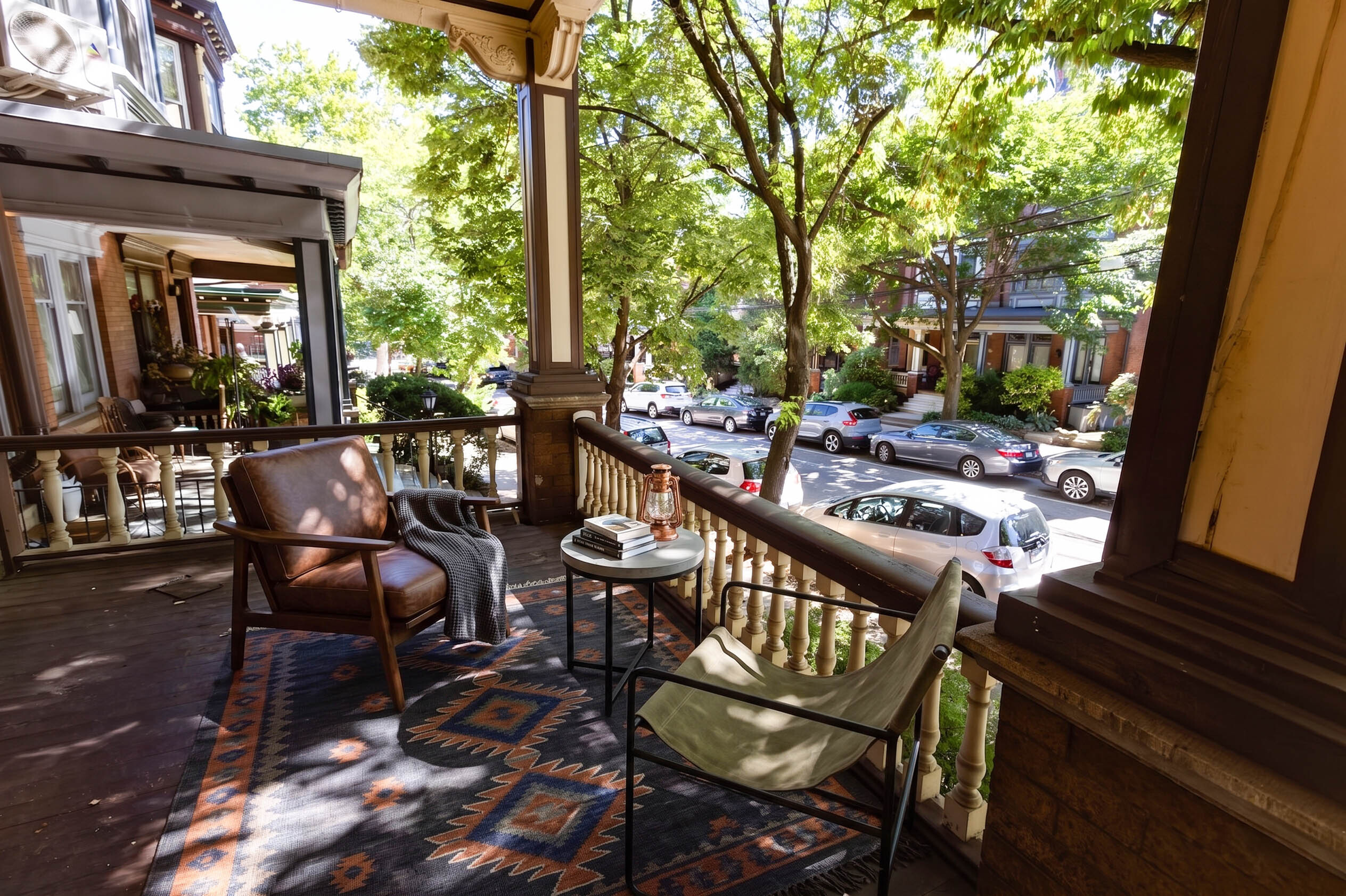 Charming outdoor porch with comfortable seating, surrounded by lush greenery, offering a serene view of the tree-lined street below.