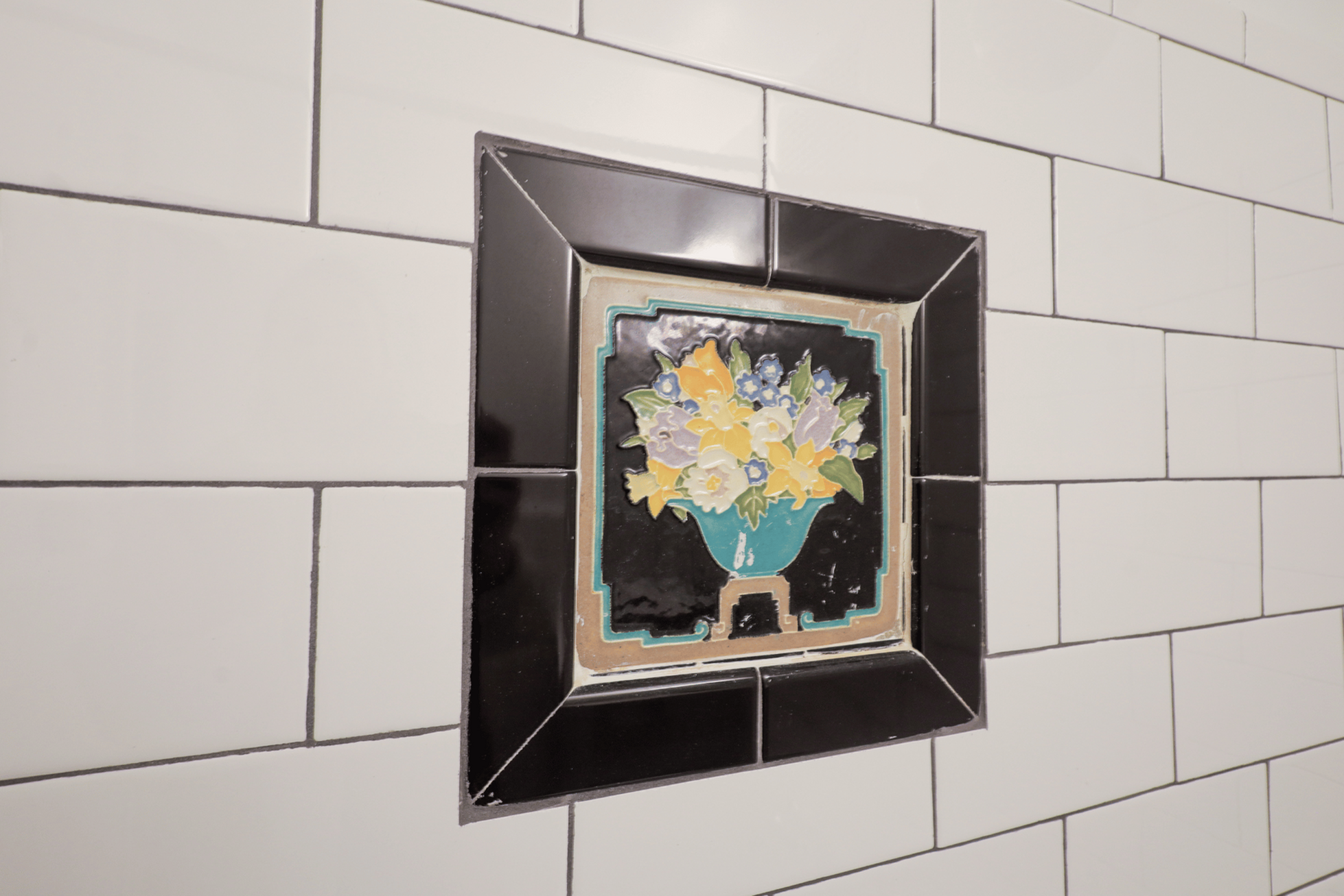 Chic bathroom tile featuring a vibrant floral design in a decorative frame, set against classic white subway tiles.