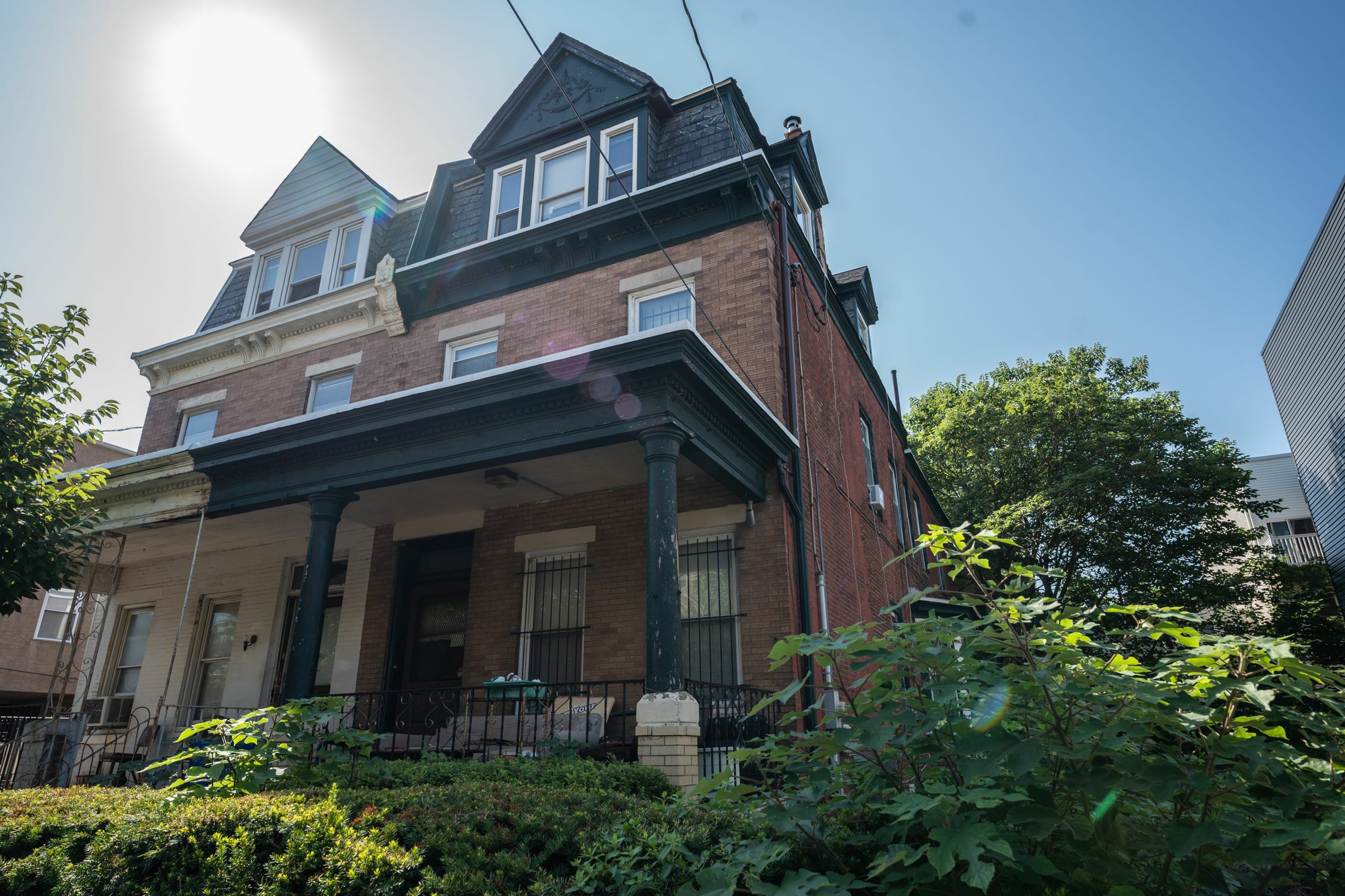 Charming three-story brick townhouse with classic architectural details, welcoming porch, and lush greenery under a bright blue sky.
