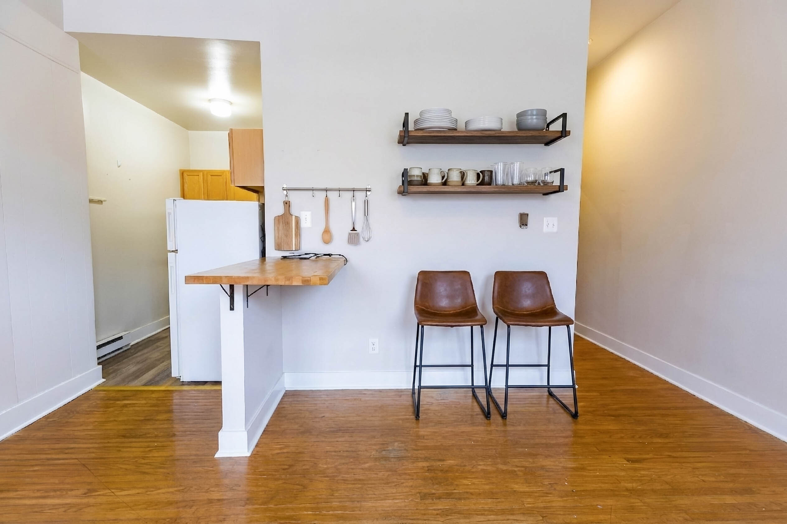 Modern kitchen nook featuring wooden bar counter, stylish shelving, chic bar stools, and cozy atmosphere.