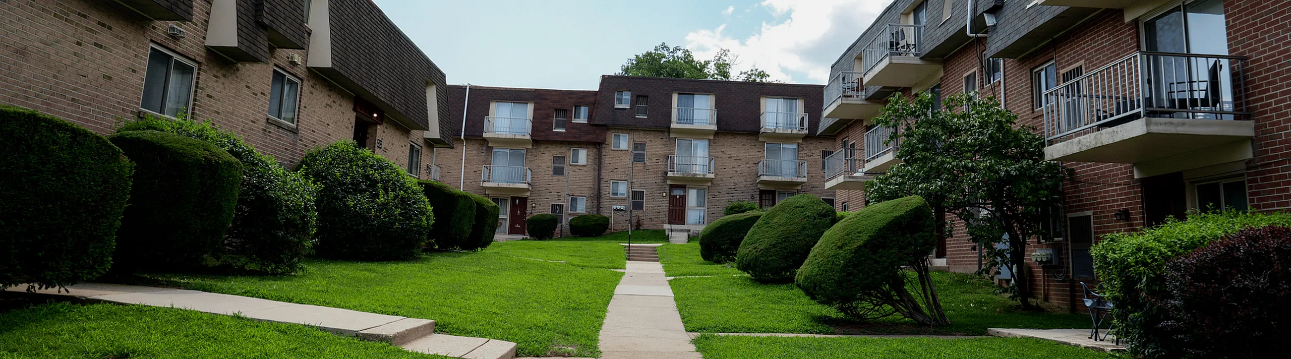 Charming apartment complex showcasing beautifully manicured lawns, elegant brick architecture, and inviting balconies under a bright sky.