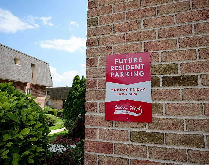 Charming residential area with future resident parking sign on a brick wall, surrounded by lush greenery and quaint architecture under a clear blue sky.