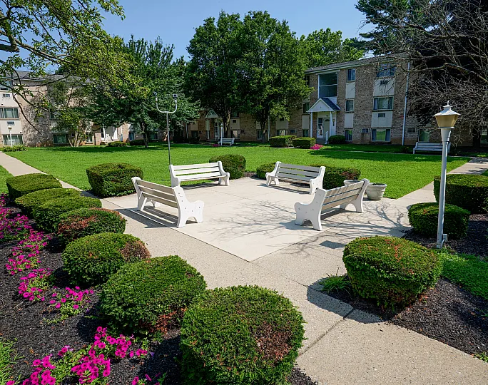 Charming apartment courtyard with lush greenery, colorful flower beds, and inviting benches for relaxation.