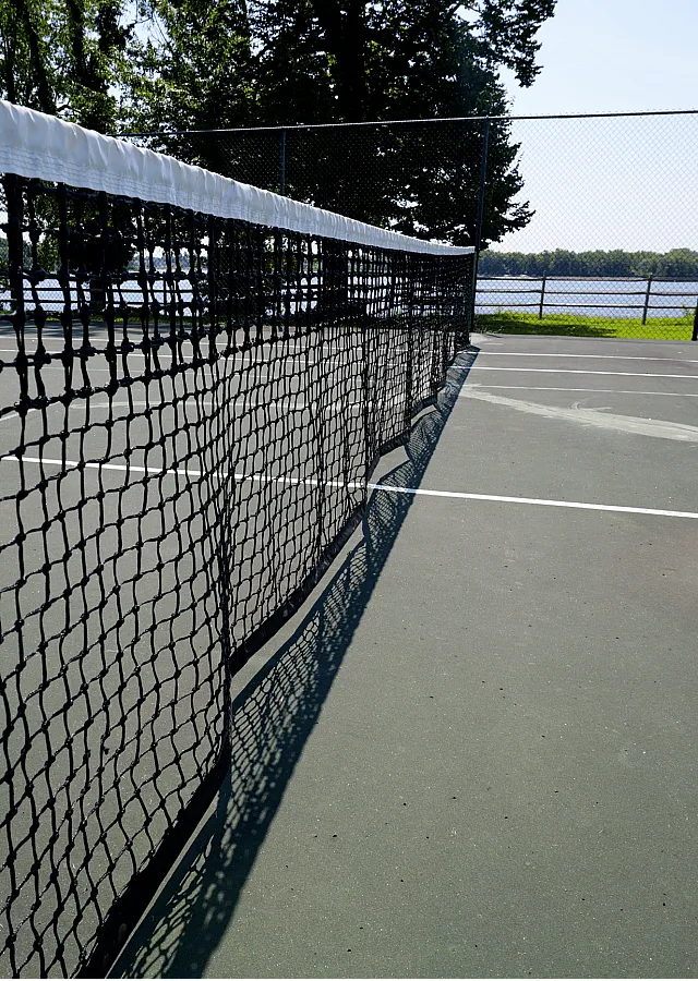 Scenic tennis court with pristine net and lush greenery, offering a serene lakeside sports experience.