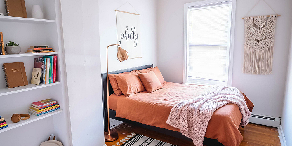Cozy bedroom with warm terracotta bedding, stylish wall art, and a sleek bookshelf filled with colorful books.
