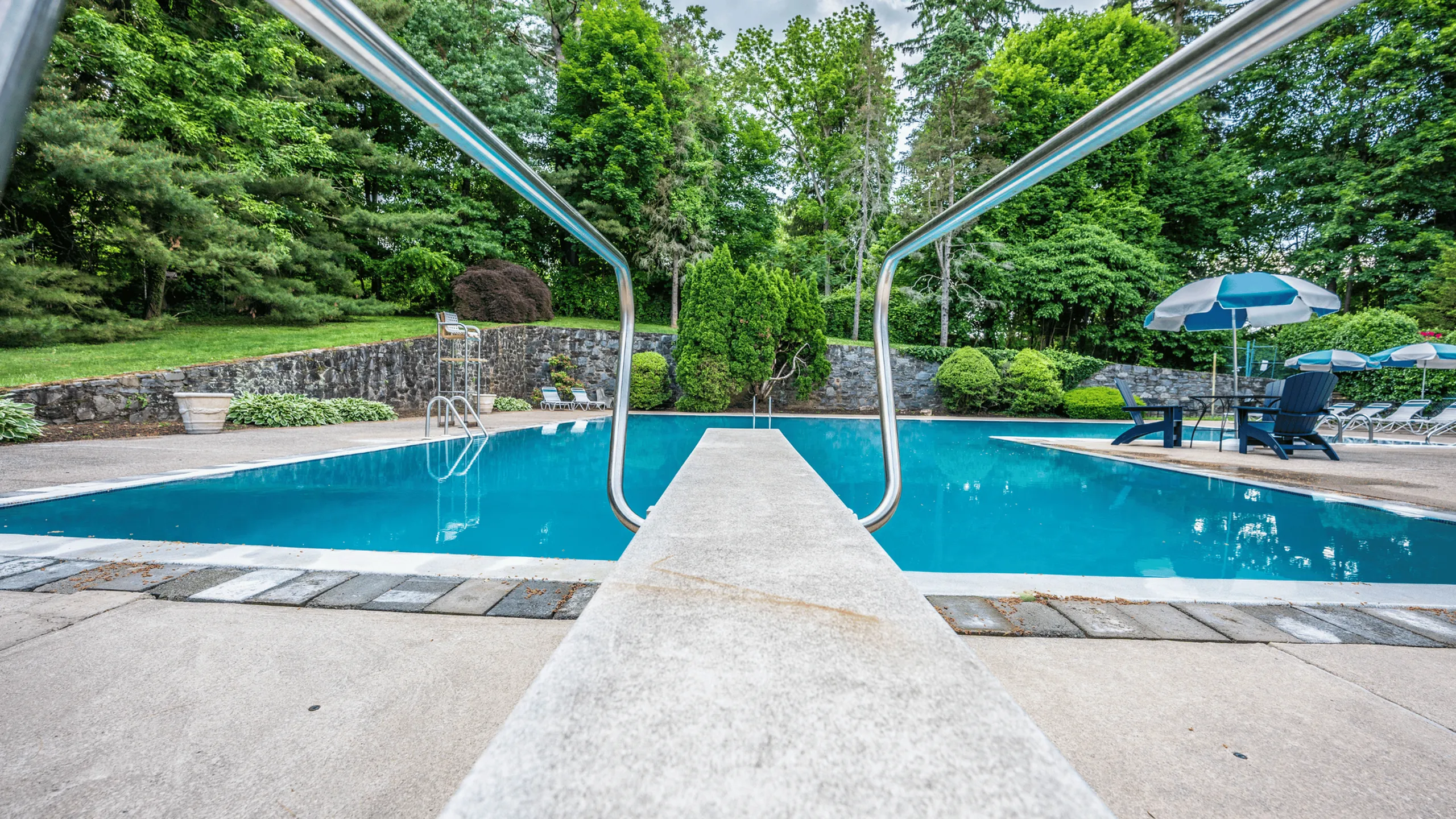 Inviting swimming pool area with lush greenery, comfortable lounge chairs, and an umbrella-shaded table, perfect for relaxation and leisurely afternoons.