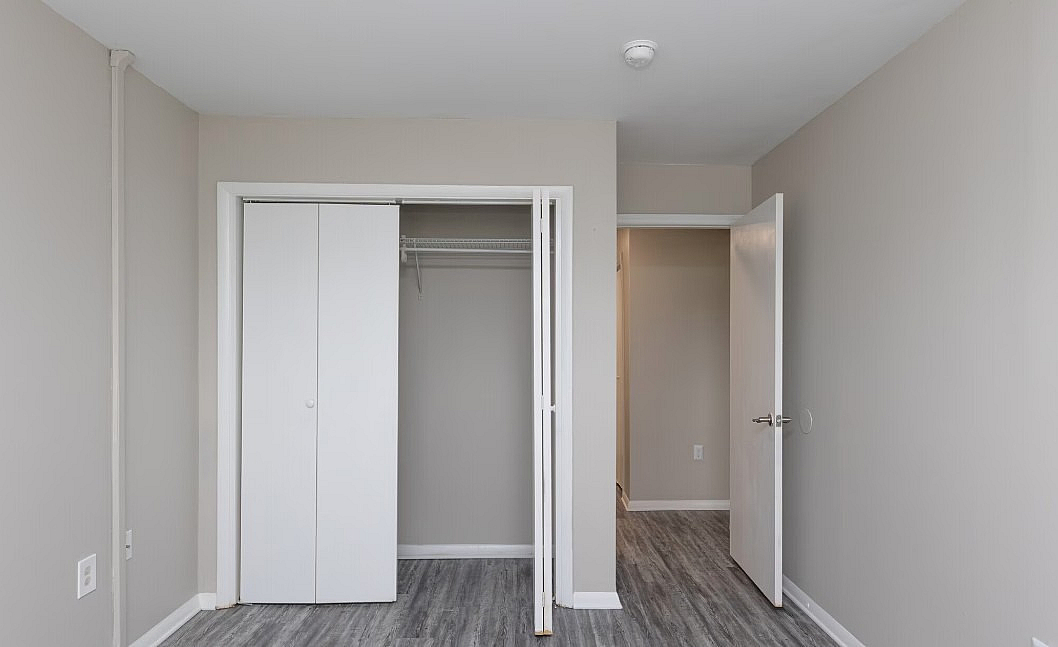 Modern bedroom with elegant gray flooring, spacious closet, and sleek white doors offering a minimalist and inviting atmosphere.
