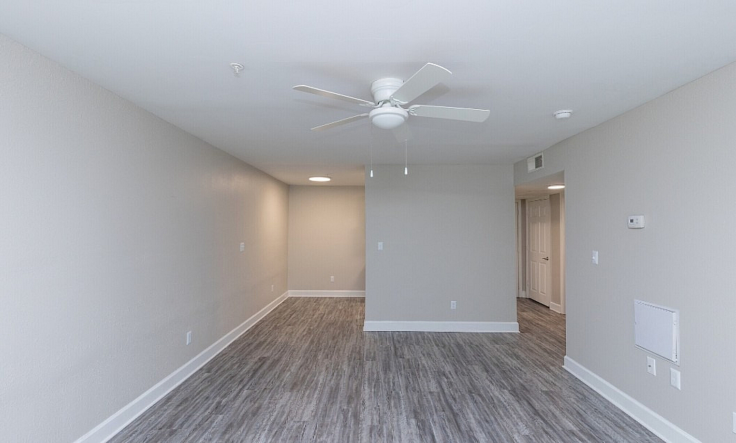 Contemporary apartment interior with sleek laminate flooring and ceiling fan, featuring ample natural light and neutral-toned walls.