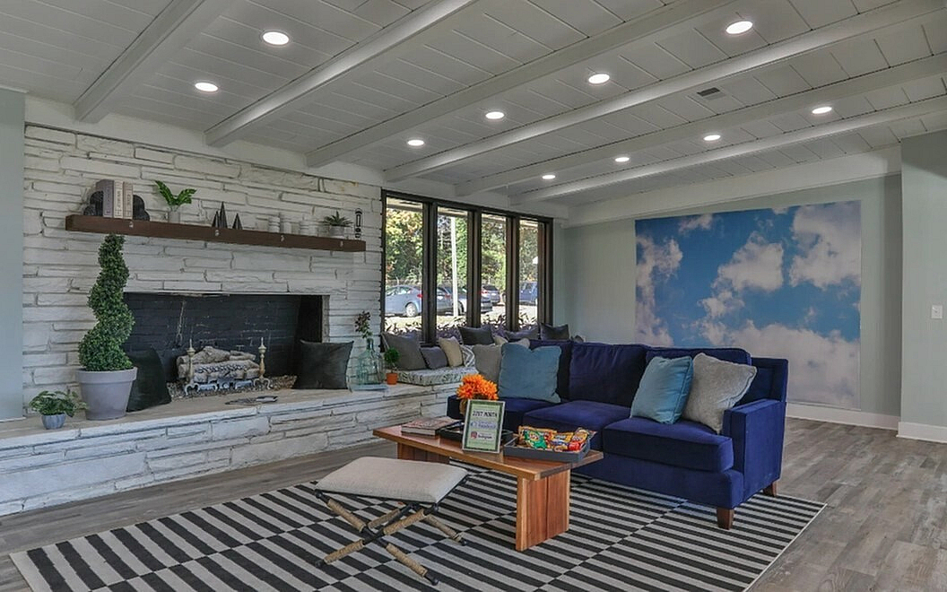 Modern living room with a cozy stone fireplace, vibrant blue sofa, and skylight-inspired wall decor, perfect for relaxing and entertaining.