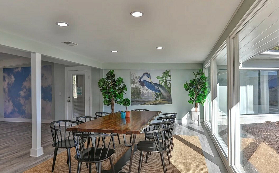 Bright dining area with a sleek wooden table, modern chairs, and vibrant wall art, surrounded by large windows allowing natural light to flood the space.