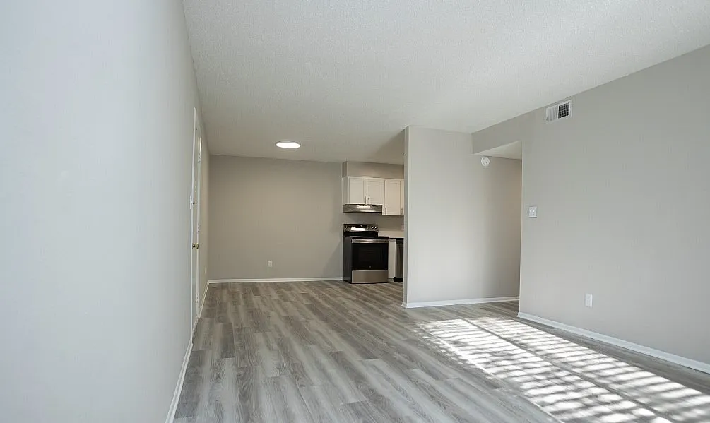 Modern apartment interior showcasing a bright, open-concept space with sleek laminate flooring and a contemporary kitchen in the background.