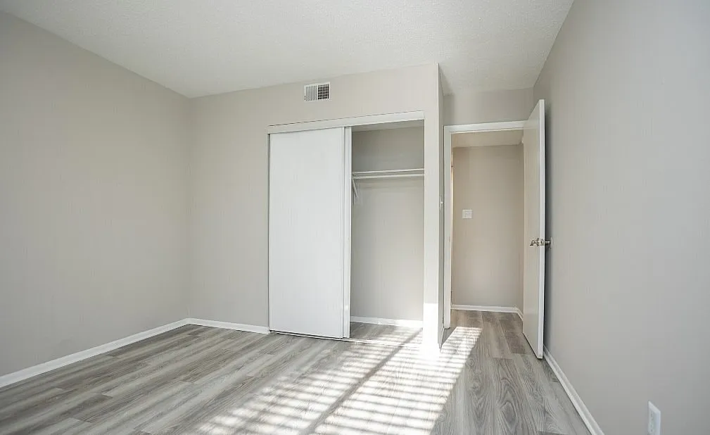 Bright, airy bedroom with sleek laminate flooring and spacious closet, perfect for modern living.