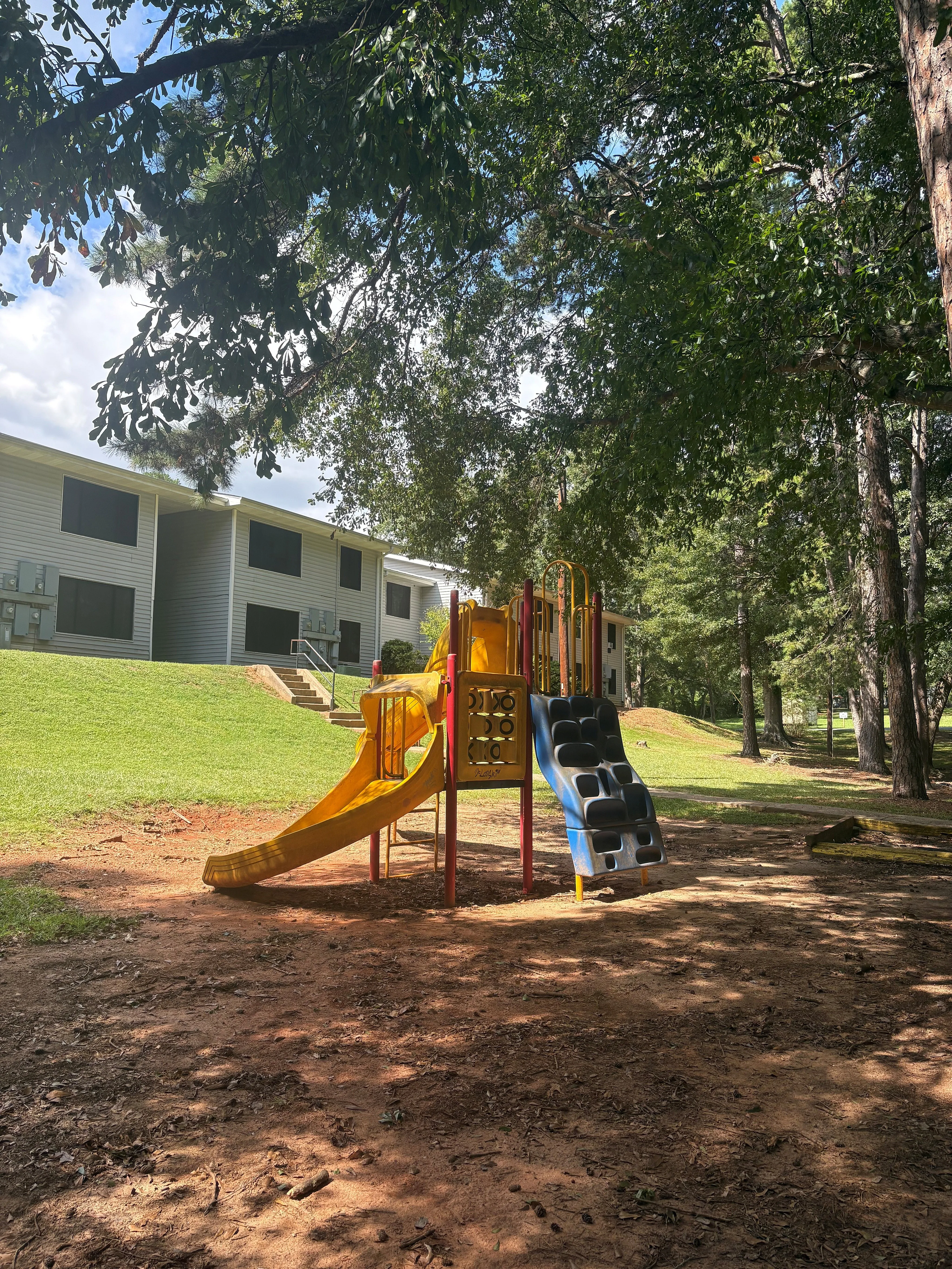 Charming apartment complex with a vibrant playground surrounded by lush greenery, perfect for family living.