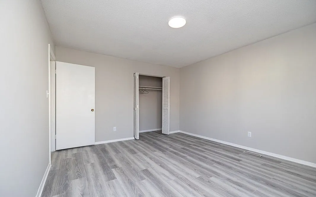 Bright and spacious bedroom with sleek wood flooring and an open closet, perfect for modern living.