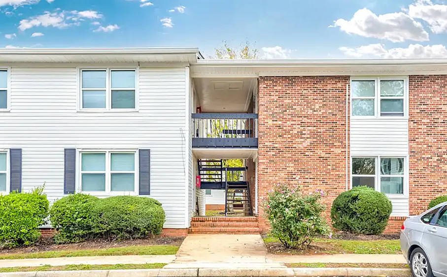 Charming brick and siding apartment building with manicured shrubs and spacious entry in a serene neighborhood setting.