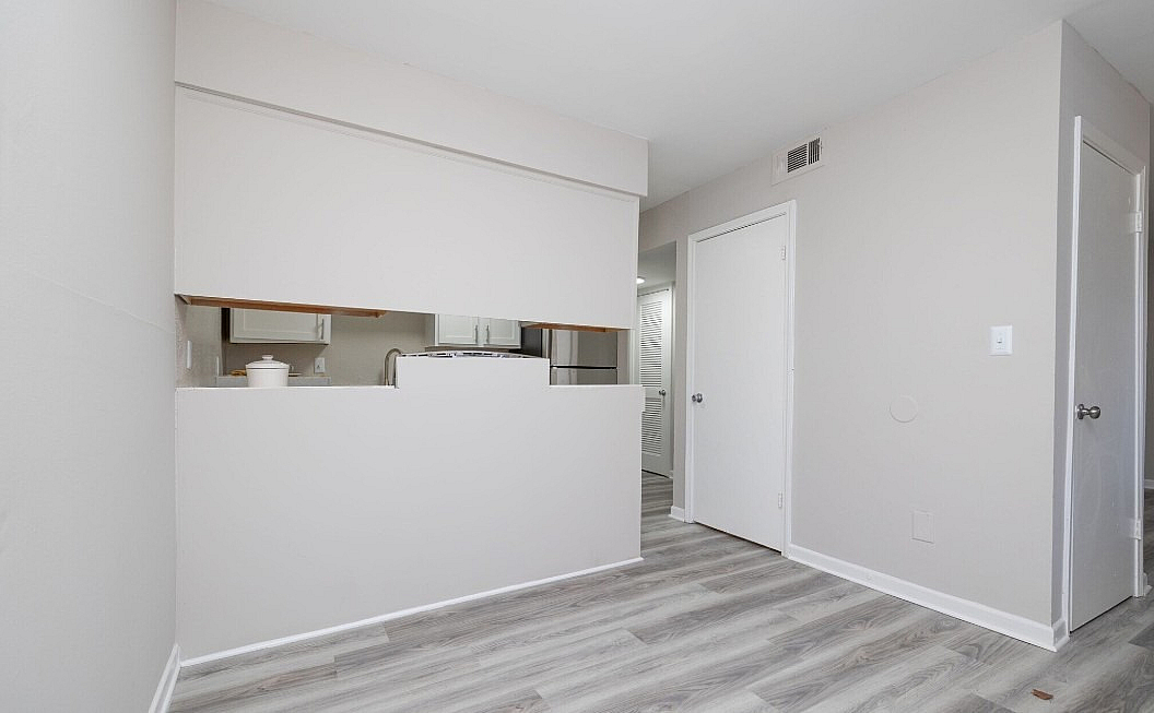 Modern apartment space with sleek laminate flooring, open pass-through to kitchen, and neutral wall tones.