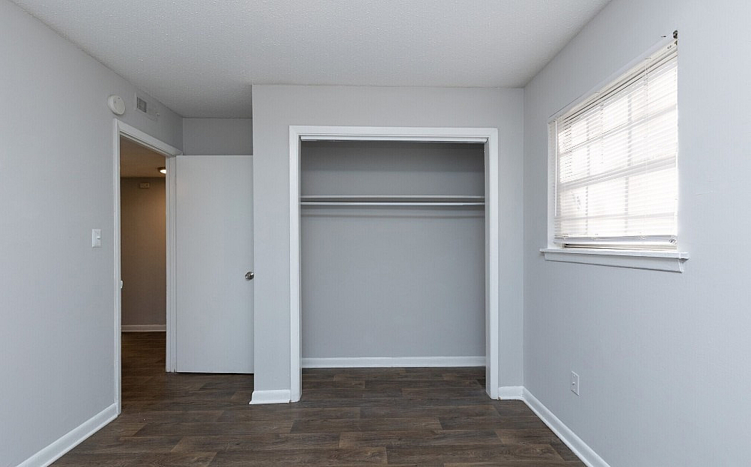 Bright room with sleek wooden flooring, white closet space, and large window offering natural light.