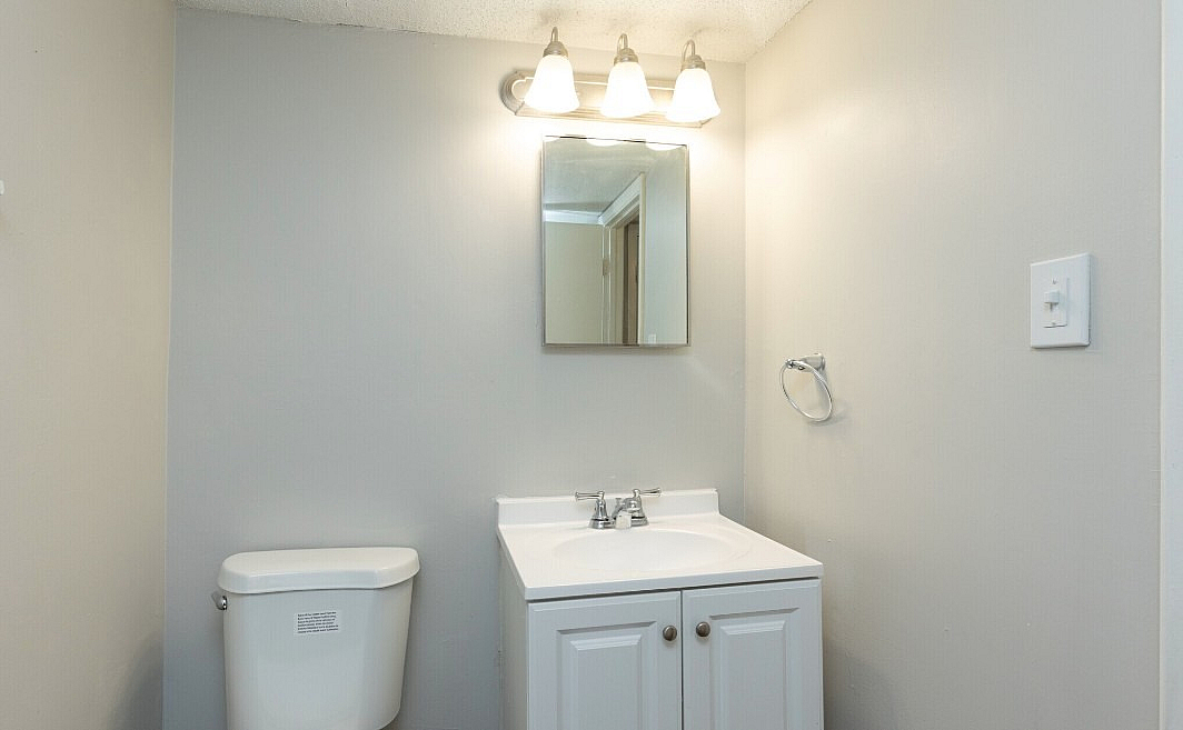 Modern bathroom featuring elegant lighting, a pristine sink with cabinetry, and a classic white toilet.