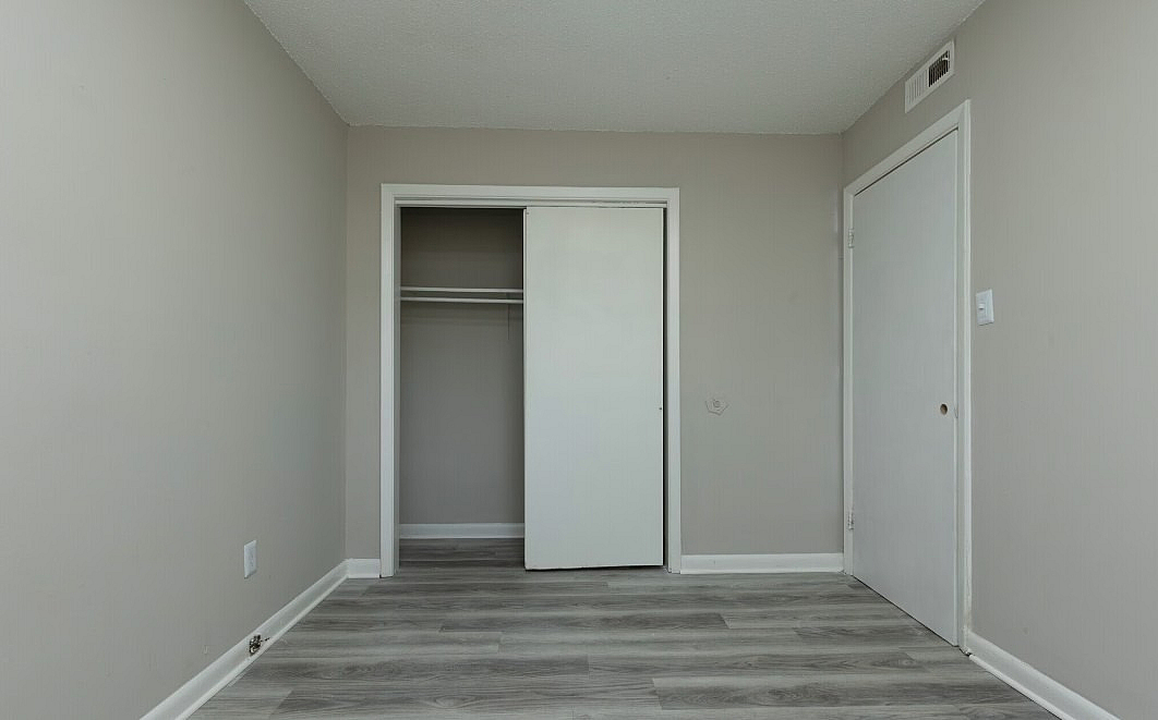 Modern, minimalist bedroom with sleek gray flooring and a built-in closet, offering ample storage space.