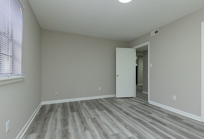 Modern and spacious room featuring sleek laminate flooring, neutral gray walls, and ample natural light.