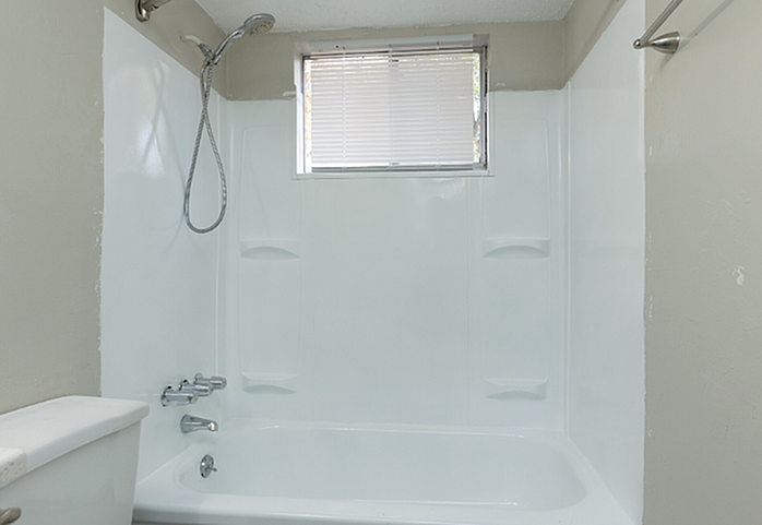 Elegant bathroom featuring a pristine white bathtub with overhead shower, complemented by natural light from the window.