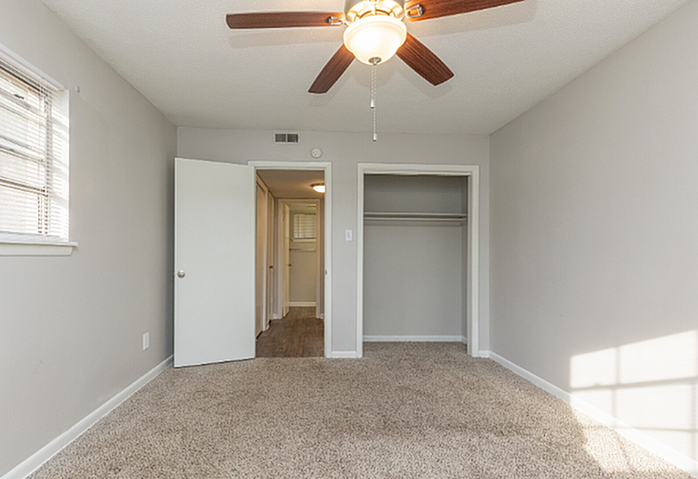 Inviting bedroom with plush carpet, ceiling fan, and ample natural light, perfect for relaxation and comfort.