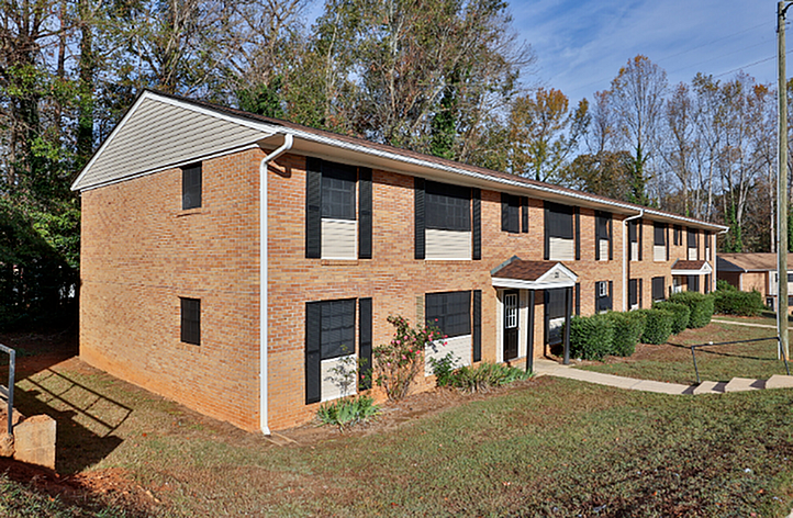 Charming brick apartment building with classic architecture and lush greenery, offering serene living in a peaceful neighborhood.