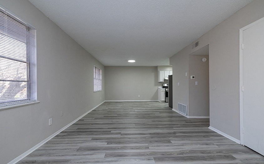 Spacious and bright open-plan living area with modern flooring and large windows, leading to a sleek kitchen.