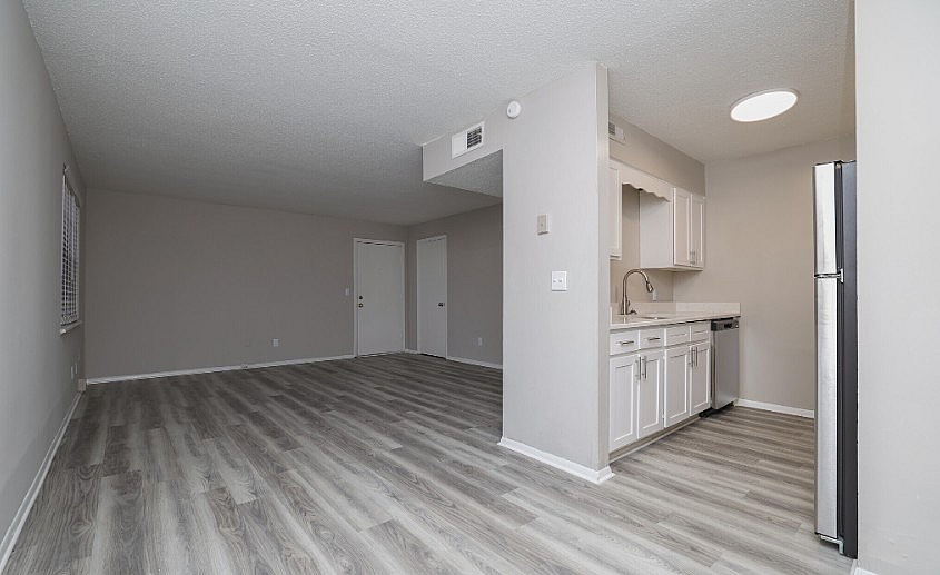 Modern open-plan living space with stylish wood flooring and a sleek white kitchen, perfect for cozy gatherings.