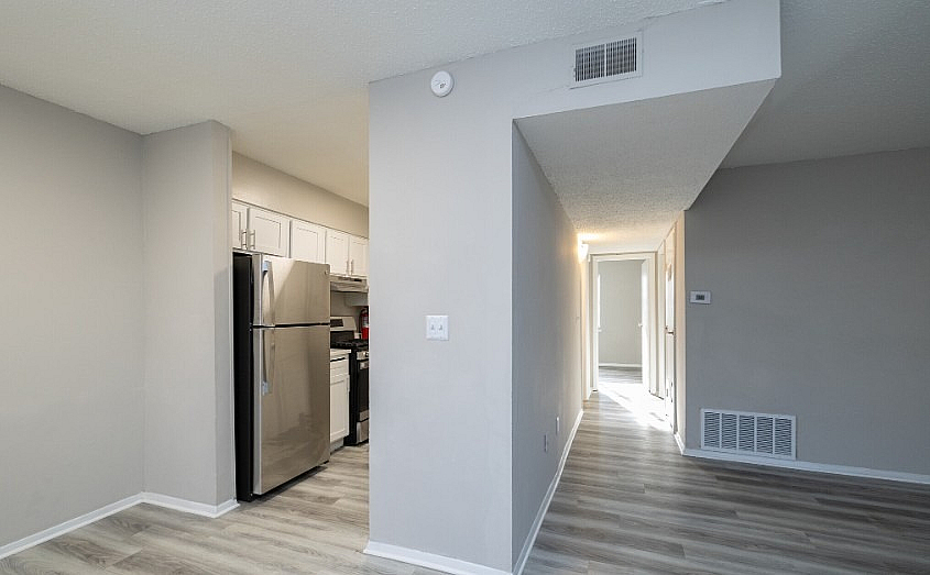 Modern apartment interior featuring a sleek stainless steel kitchen next to a bright hallway with stylish gray flooring.