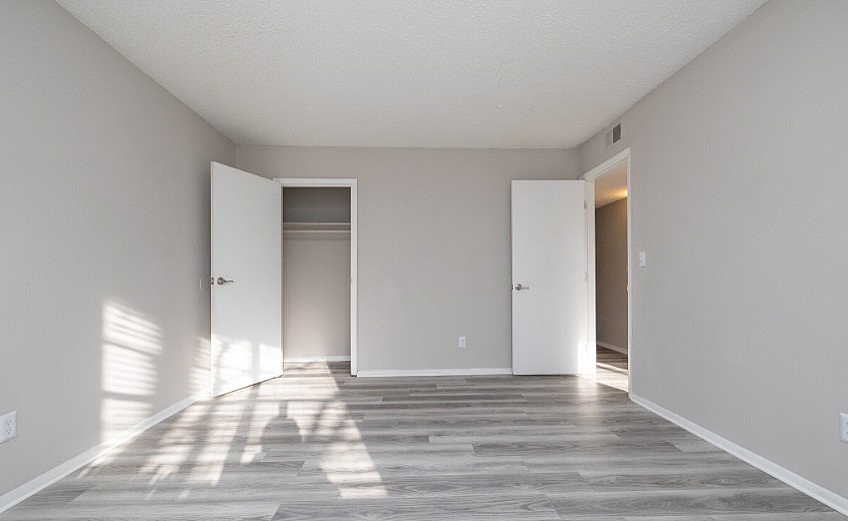 Bright and spacious bedroom with sleek gray flooring, ample natural light, and a large closet for ultimate comfort.